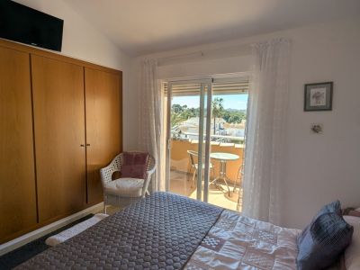 Slaapkamer met geïntegreerde houten kledingkast en toegang tot een privébalkon, met uitzicht op daken, palmbomen en verre heuvels vanaf de kleine zithoek.
