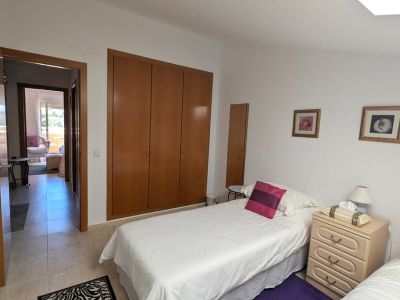 Slaapkamer met twee eenpersoonsbedden, een ingebouwde houten kledingkast en nachtkastje. Een open deur onthult een buitenterras.
