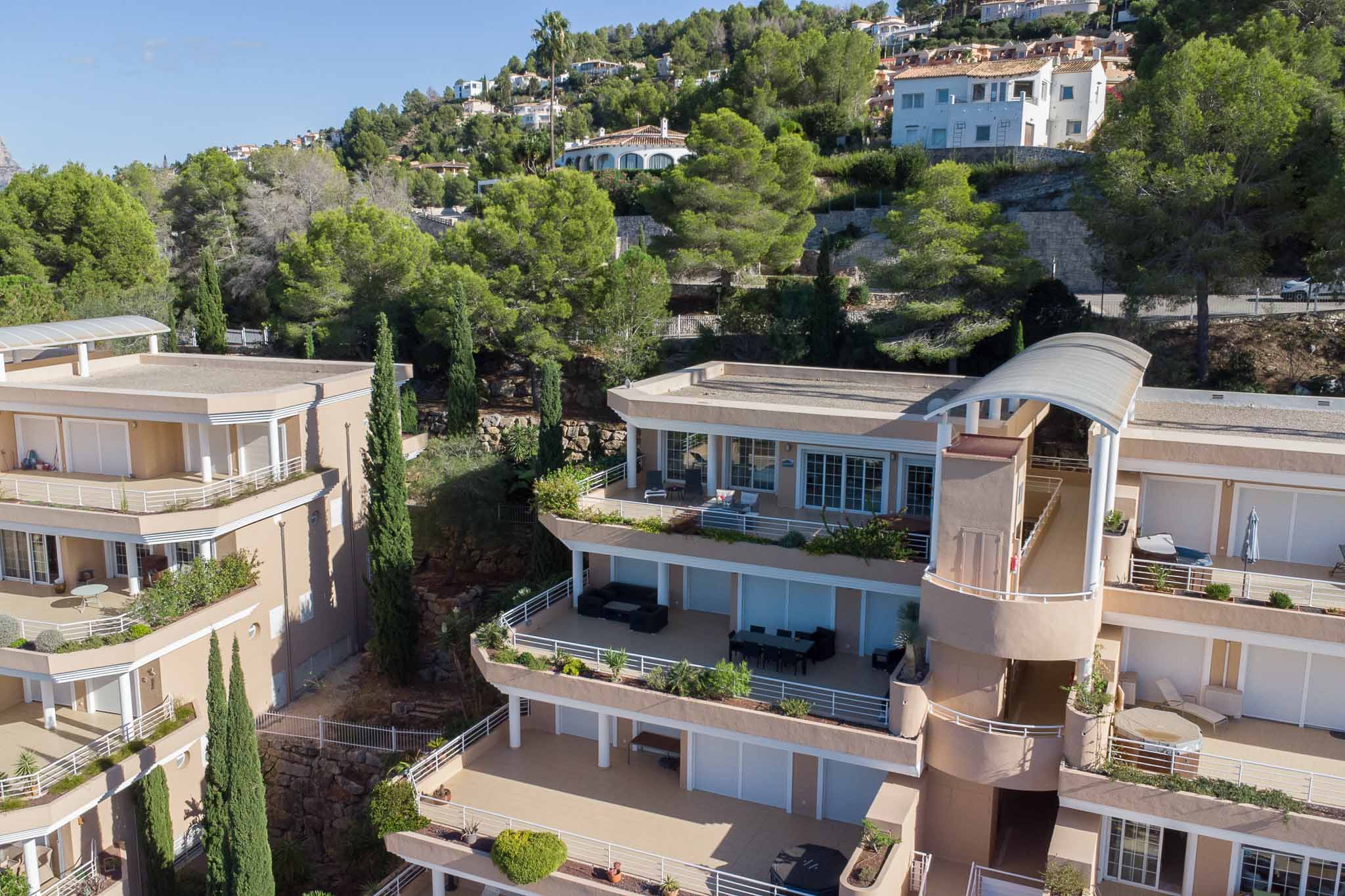 Exterieur van het Las Mimosas complex met terrasvormige architectuur, ruime privéterrassen en aardetinten gevels, geïntegreerd in de beboste heuvels van La Sella.