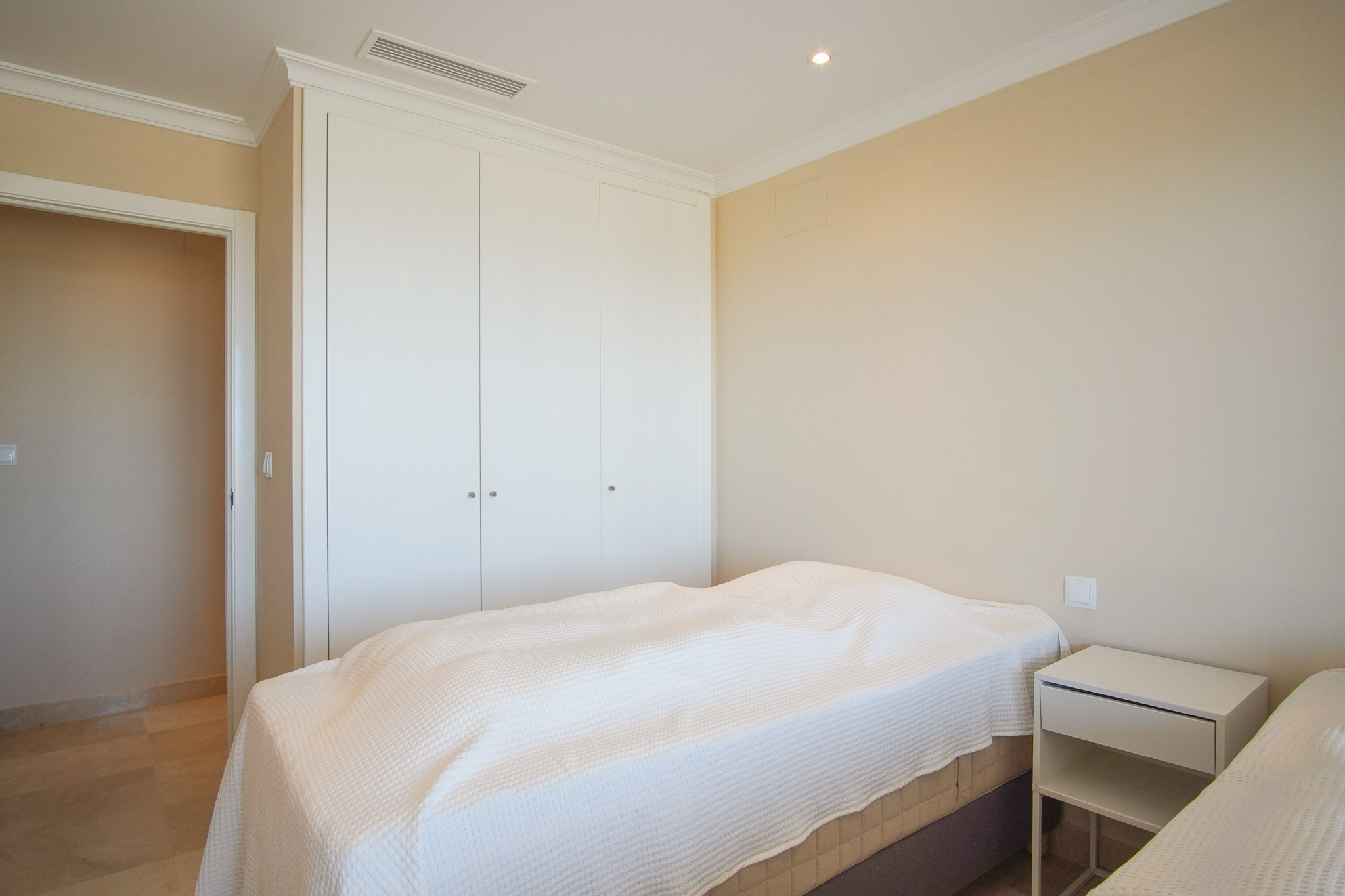 Lichte slaapkamer met witte inbouwkasten, marmeren vloer en geïntegreerde airconditioning. Crèmekleurige muren en klassieke plafondlijsten.