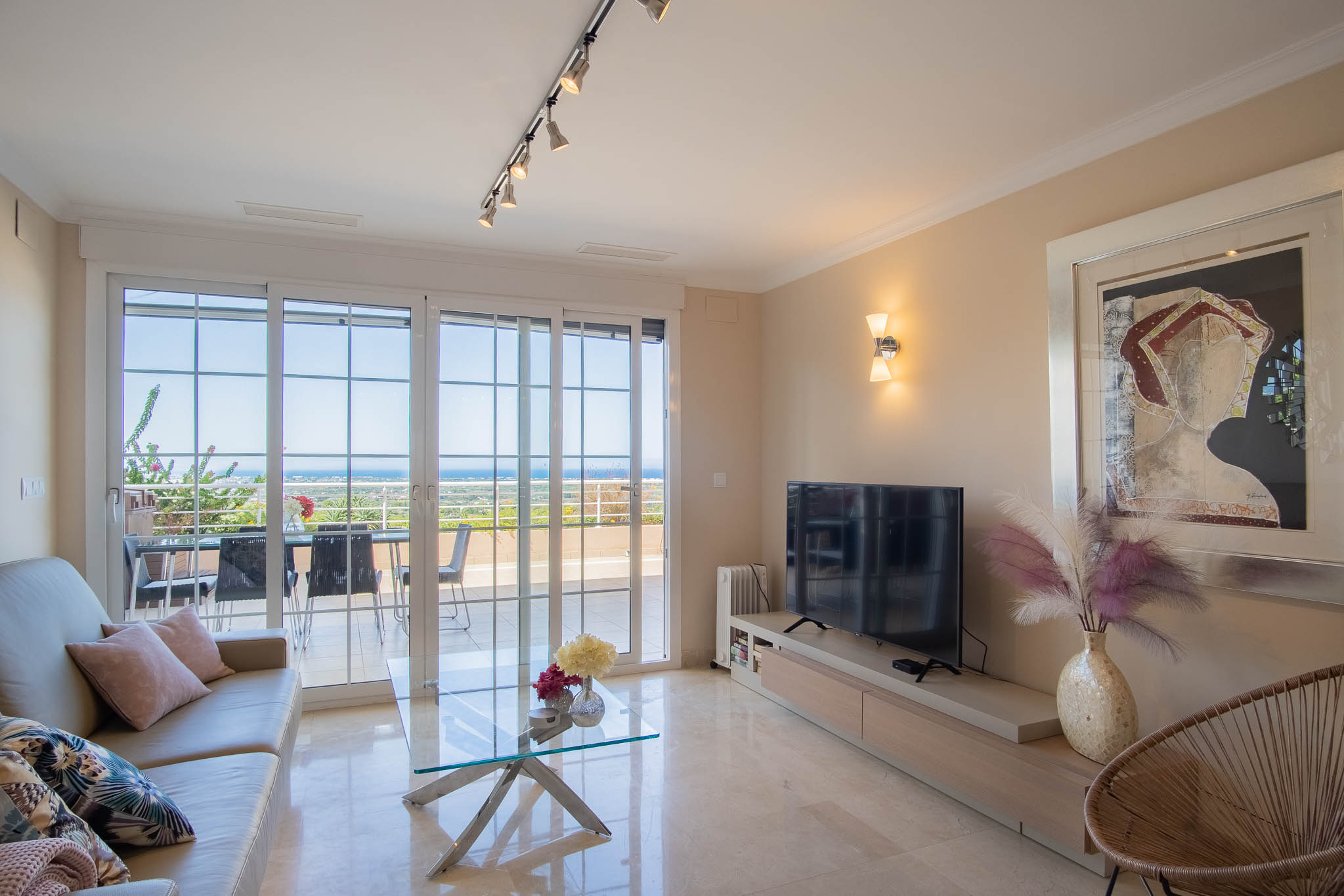 Lichte woonkamer met gepolijste marmeren vloeren, modern meubilair en grote schuifdeuren die toegang bieden tot het terras met panoramisch zeezicht.