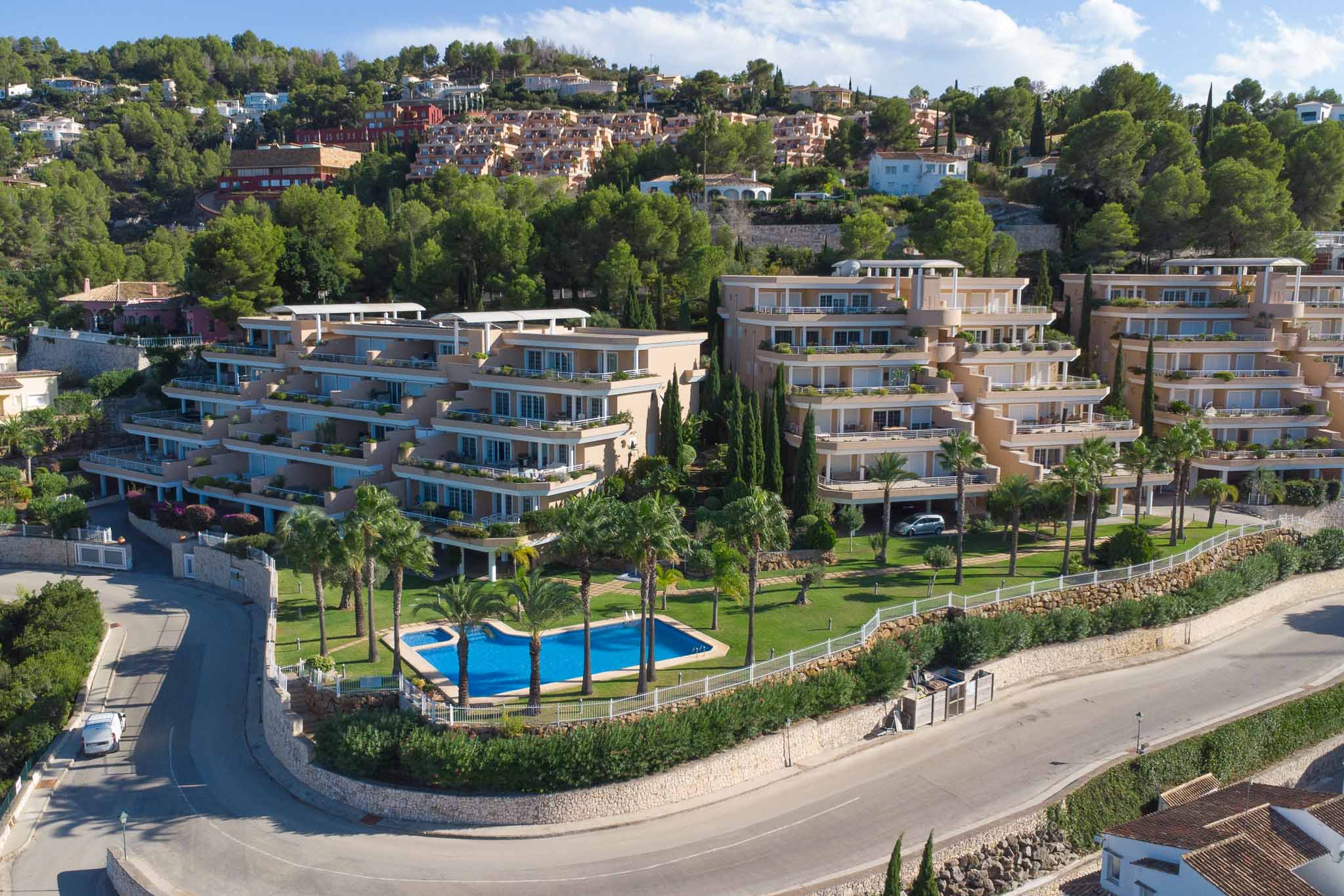 Luchtfoto van het Las Mimosas-complex in La Sella, met terrasvormige architectuur, een gemeenschappelijk zwembad met palmbomen en verzorgde tuinen.