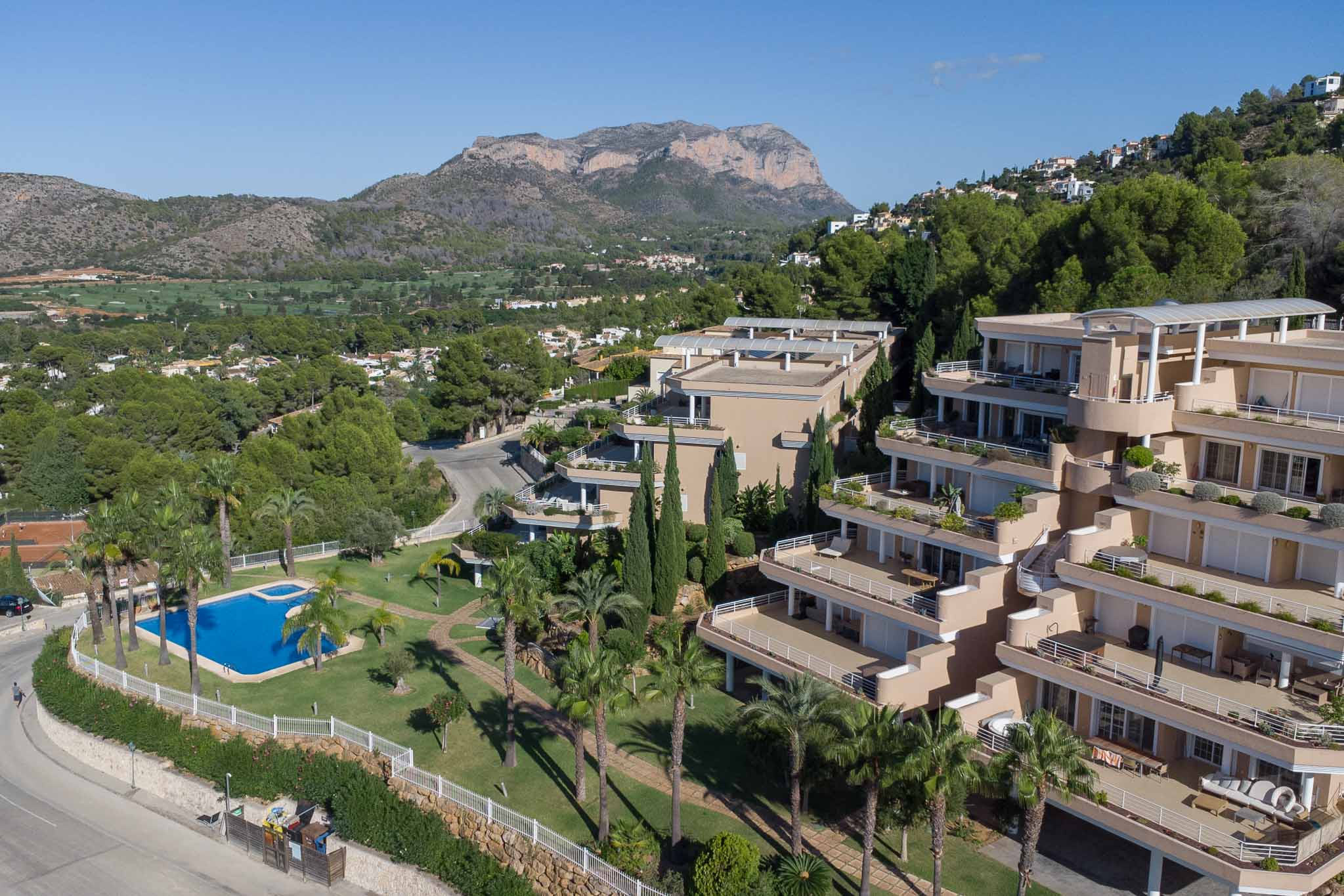 Luchtfoto van residentie Las Mimosas met het gemeenschappelijke zwembad, mediterrane tuinen en terraswoningen met uitzicht op de golfbaan en de Montgó.