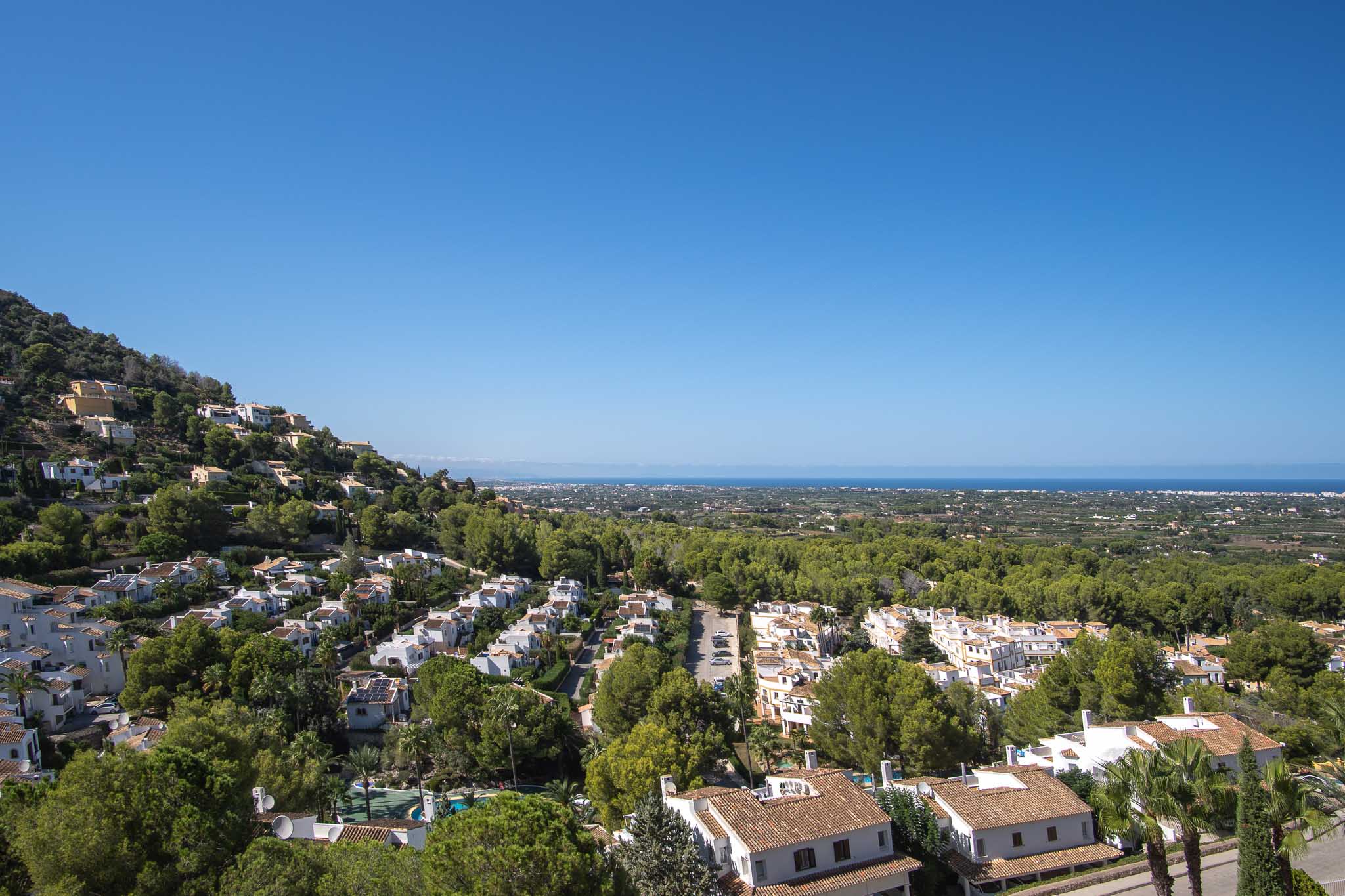 Panoramisch uitzicht vanuit La Sella op de Middellandse Zee, met residentiële architectuur geïntegreerd in een weelderige groene omgeving onder een heldere hemel.