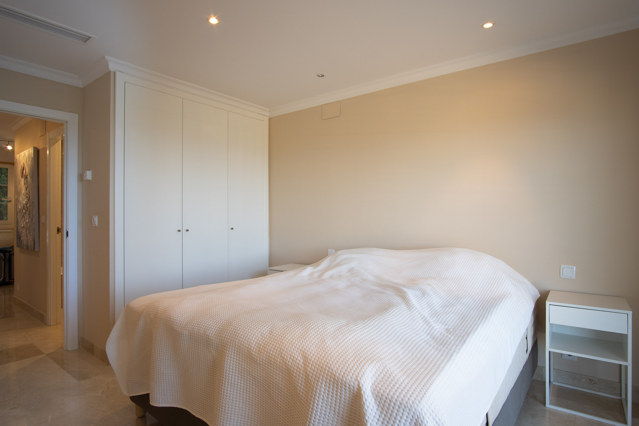 Slaapkamer met marmeren vloer, kamerhoge witte inbouwkasten en inbouwspots in het plafond, gekenmerkt door een strak en functioneel interieurontwerp.