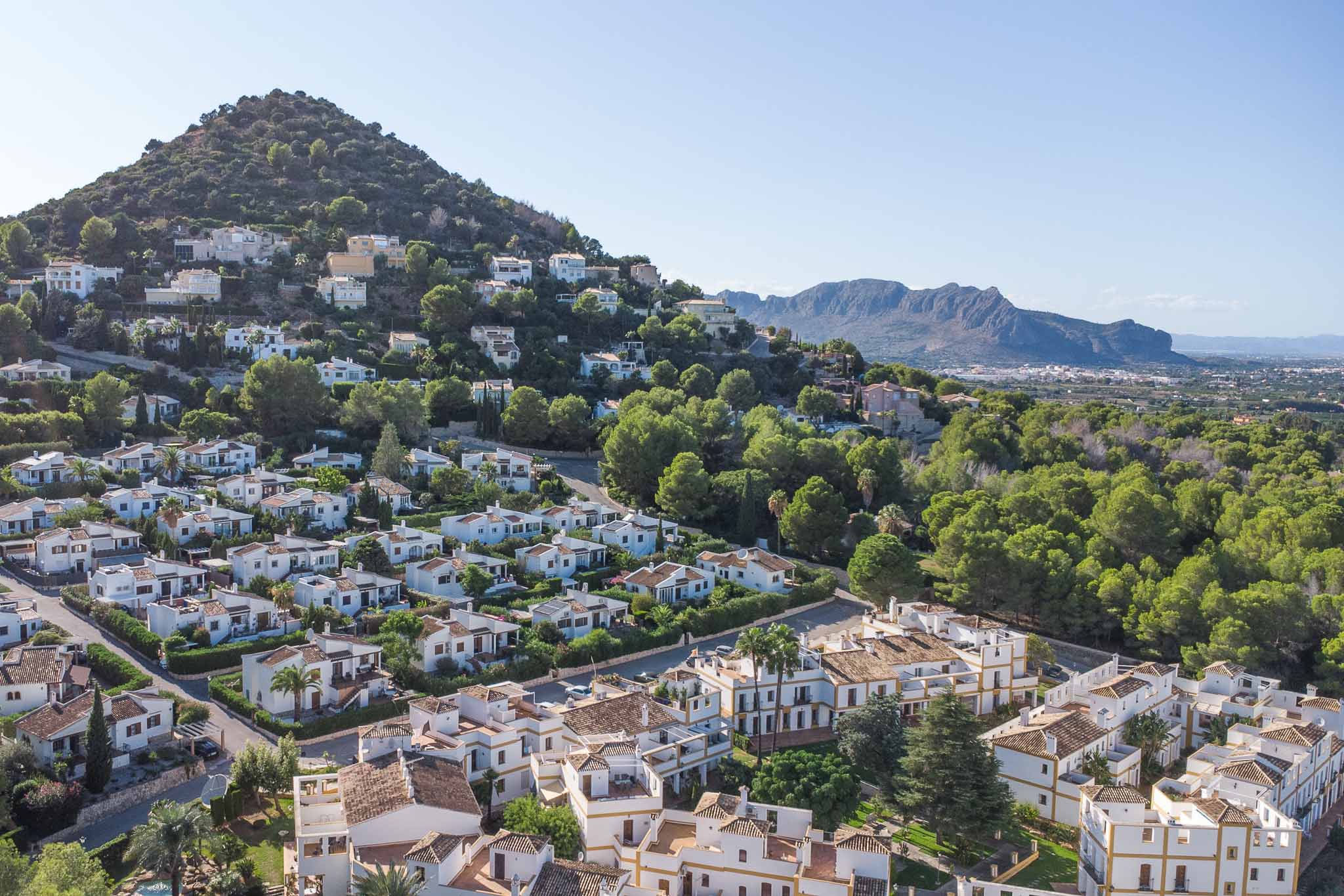 Verhoogd panoramisch uitzicht op de woonwijk La Sella, met mediterrane architectuur te midden van groene pijnbomen en een indrukwekkend berglandschap.