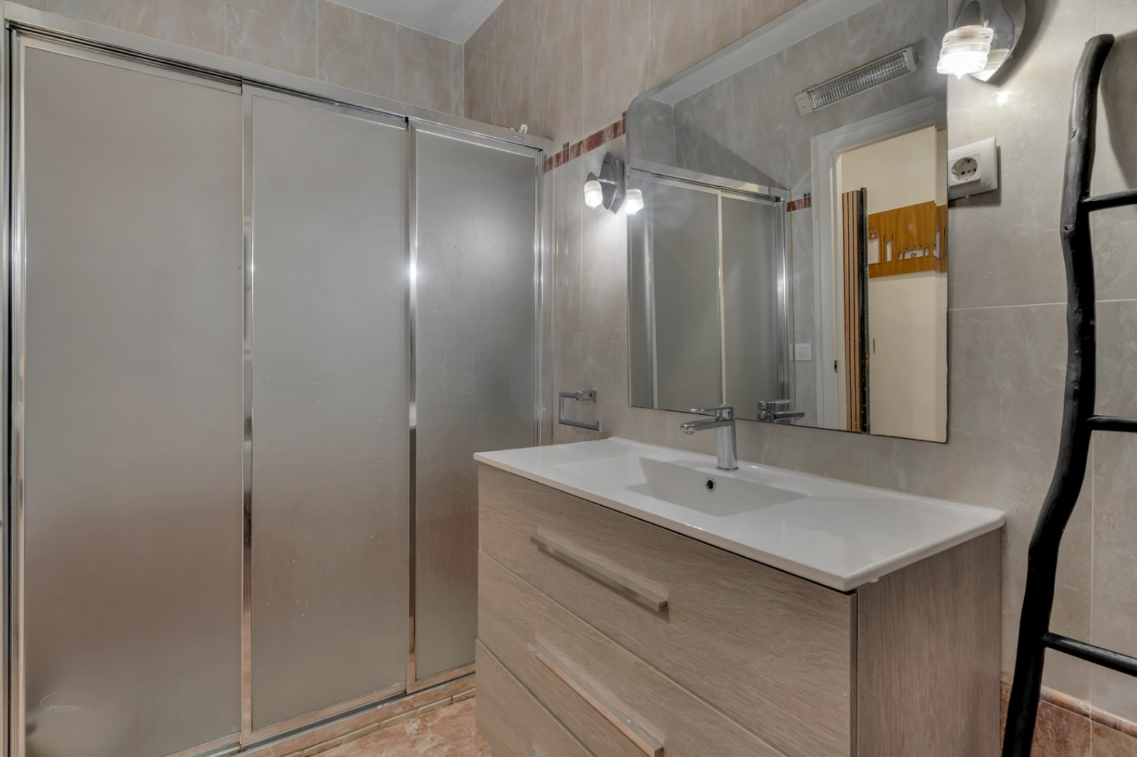 Badkamerdetail met wastafel ingebouwd in een licht houten meubel en een douche met schuifdeuren.