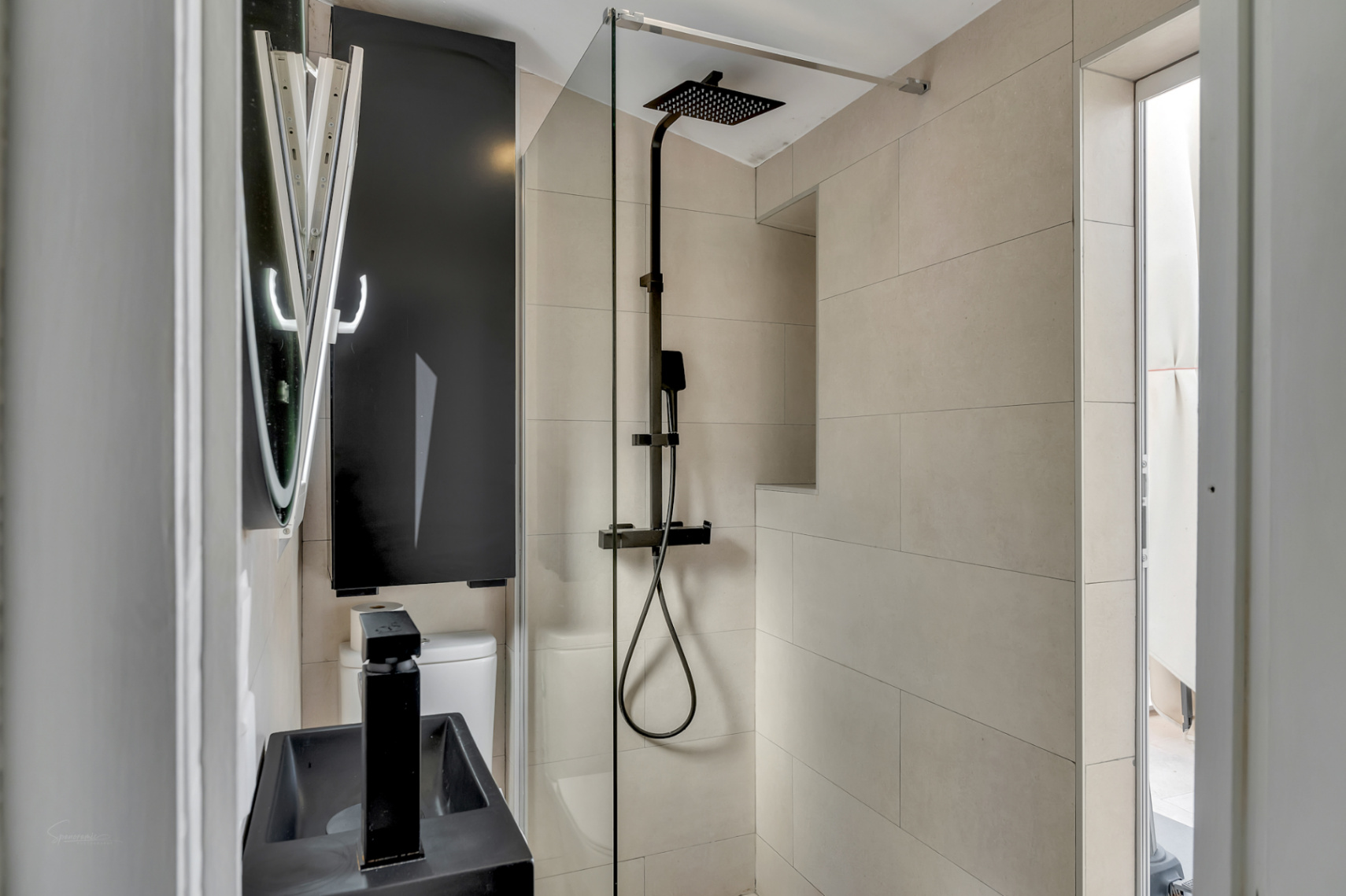 Detail van moderne badkamer met zwarte regendouche, zwarte wastafel en crèmekleurige tegels.