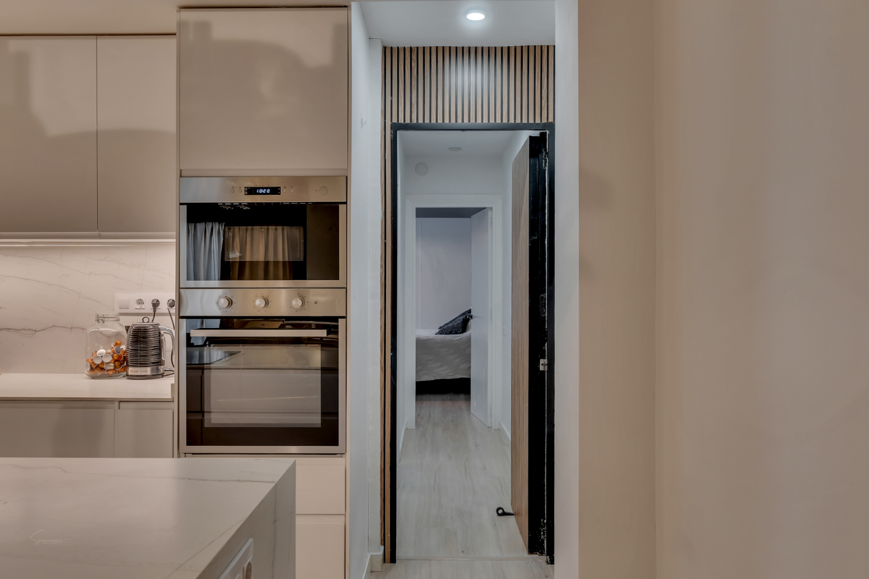 Keukendetail met ingebouwde oven en zicht op de slaapkamer door een deuropening met houten design.