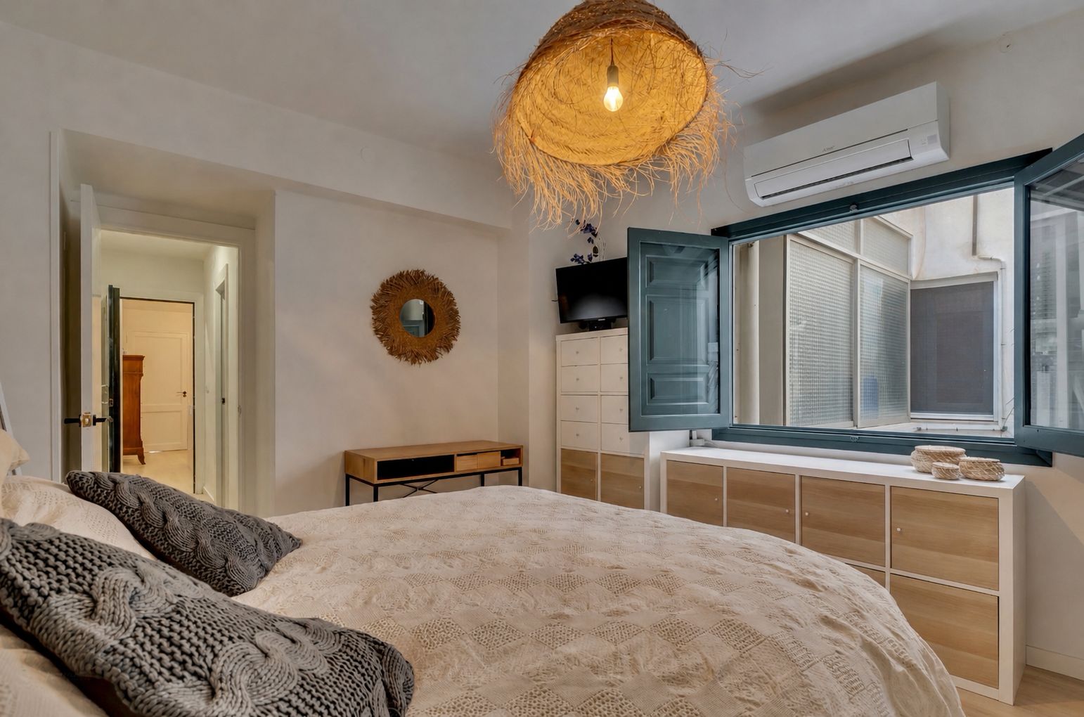Lichte slaapkamer met tweepersoonsbed, blauw houten raamkozijn en hanglamp van wicker.