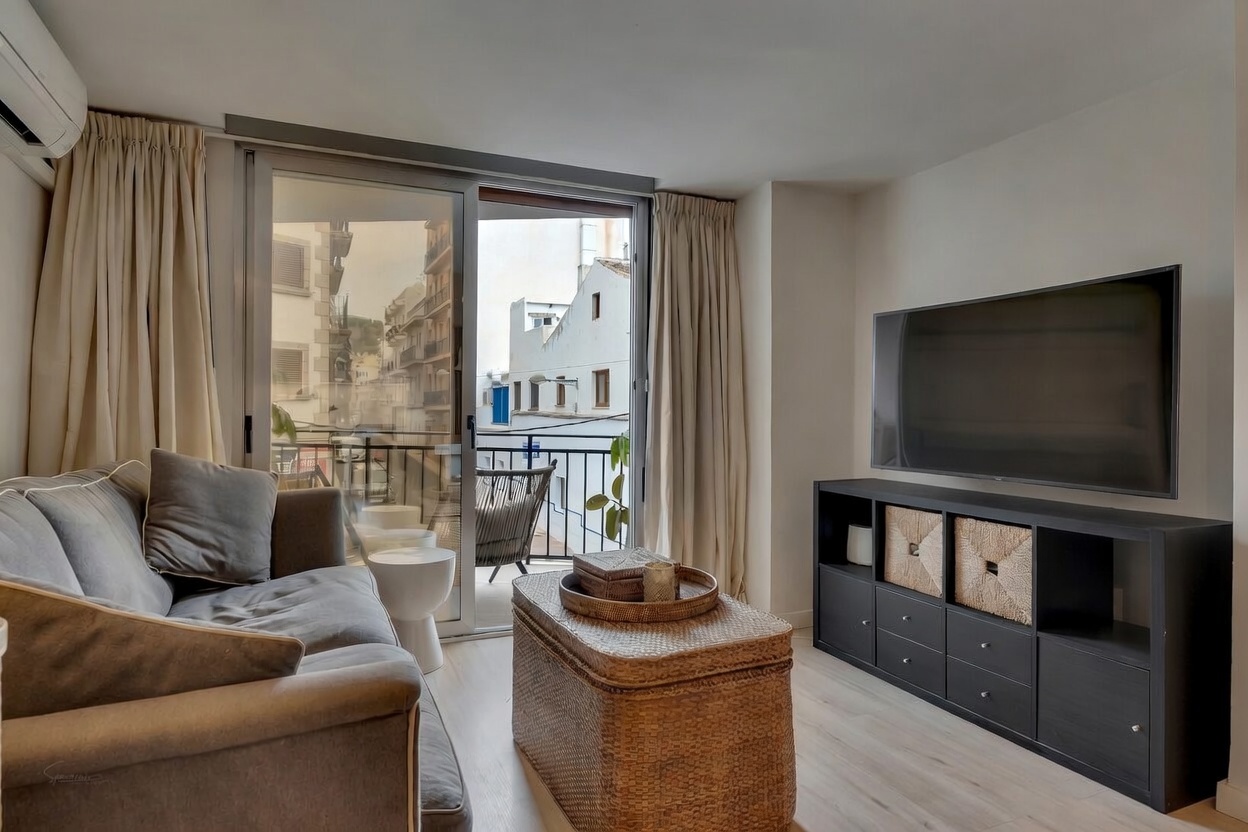 Lichte woonkamer met grijze bank, salontafel van riet en toegang tot balkon met uitzicht op de stad.