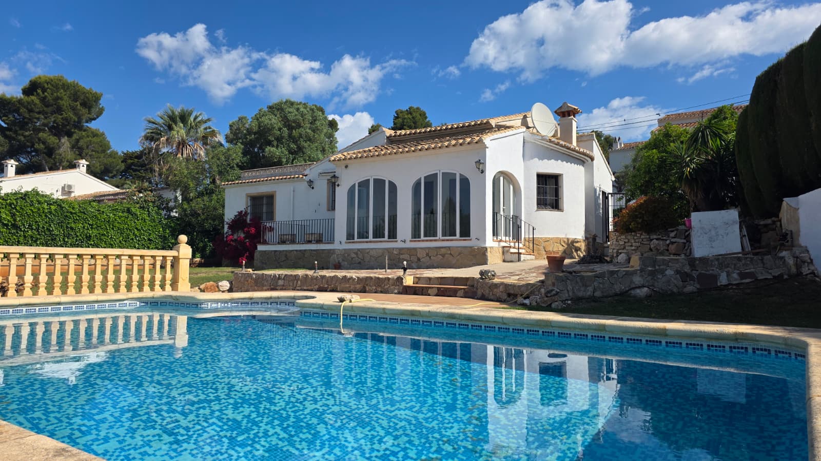 Buitenaanzicht van het privézwembad en de witte villa met karakteristieke boogramen en natuurstenen plint in de wijk El Tosalet, Jávea.