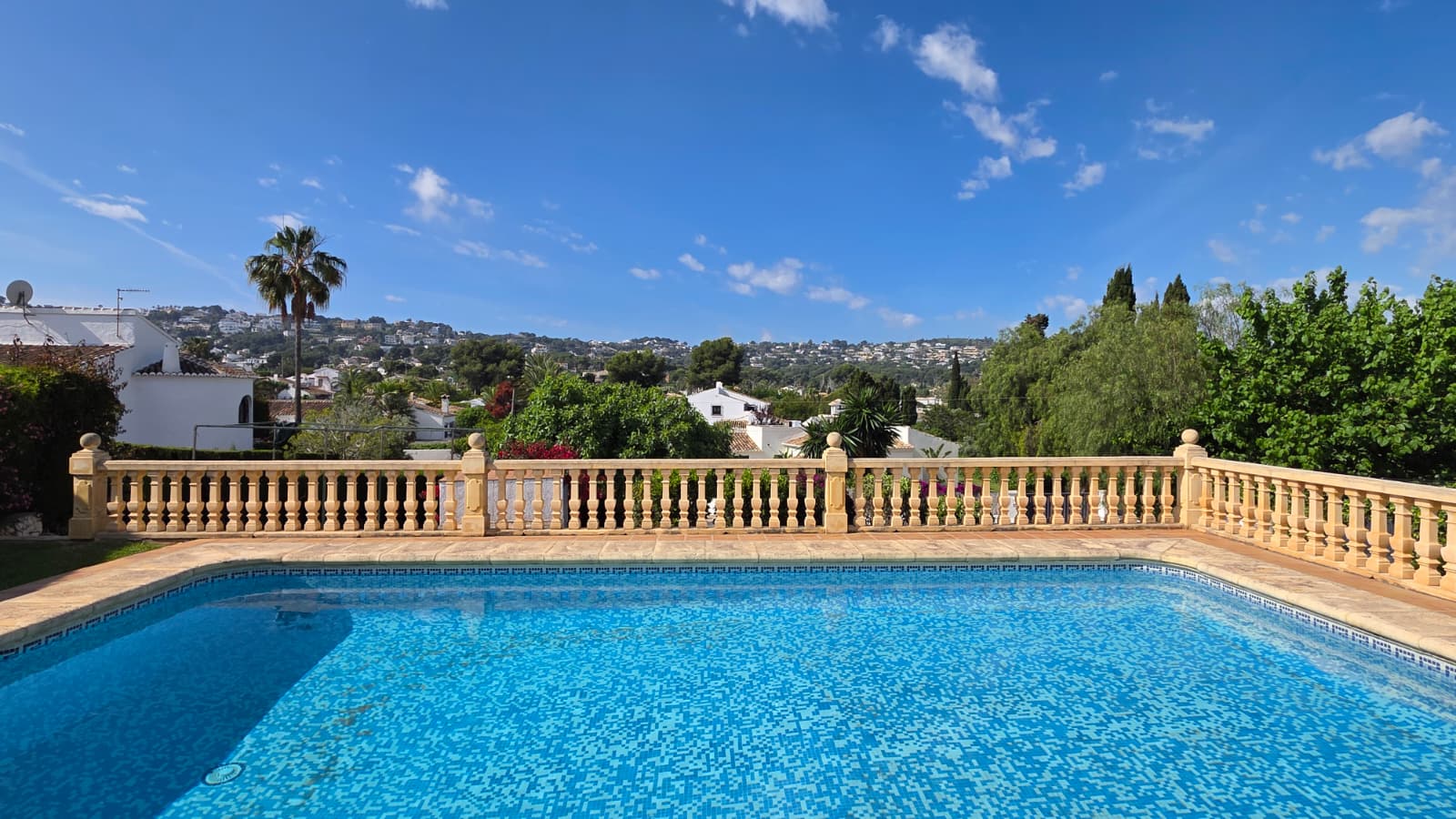 Buitenzwembad met blauwe mozaïektegels en een klassieke stenen balustrade, met vrij uitzicht over de heuvels en de woonwijk van Jávea.