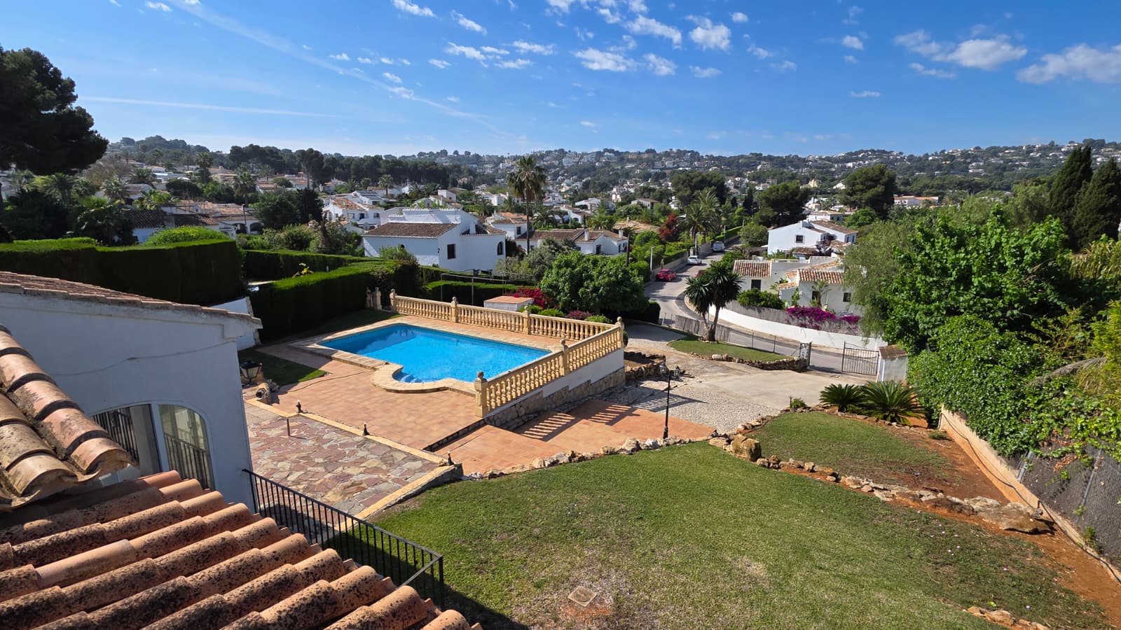 Verhoogd uitzicht op het privézwembad met stenen balustrade, terracotta terras en gazon, met weids uitzicht over de urbanisatie El Tosalet in Jávea.