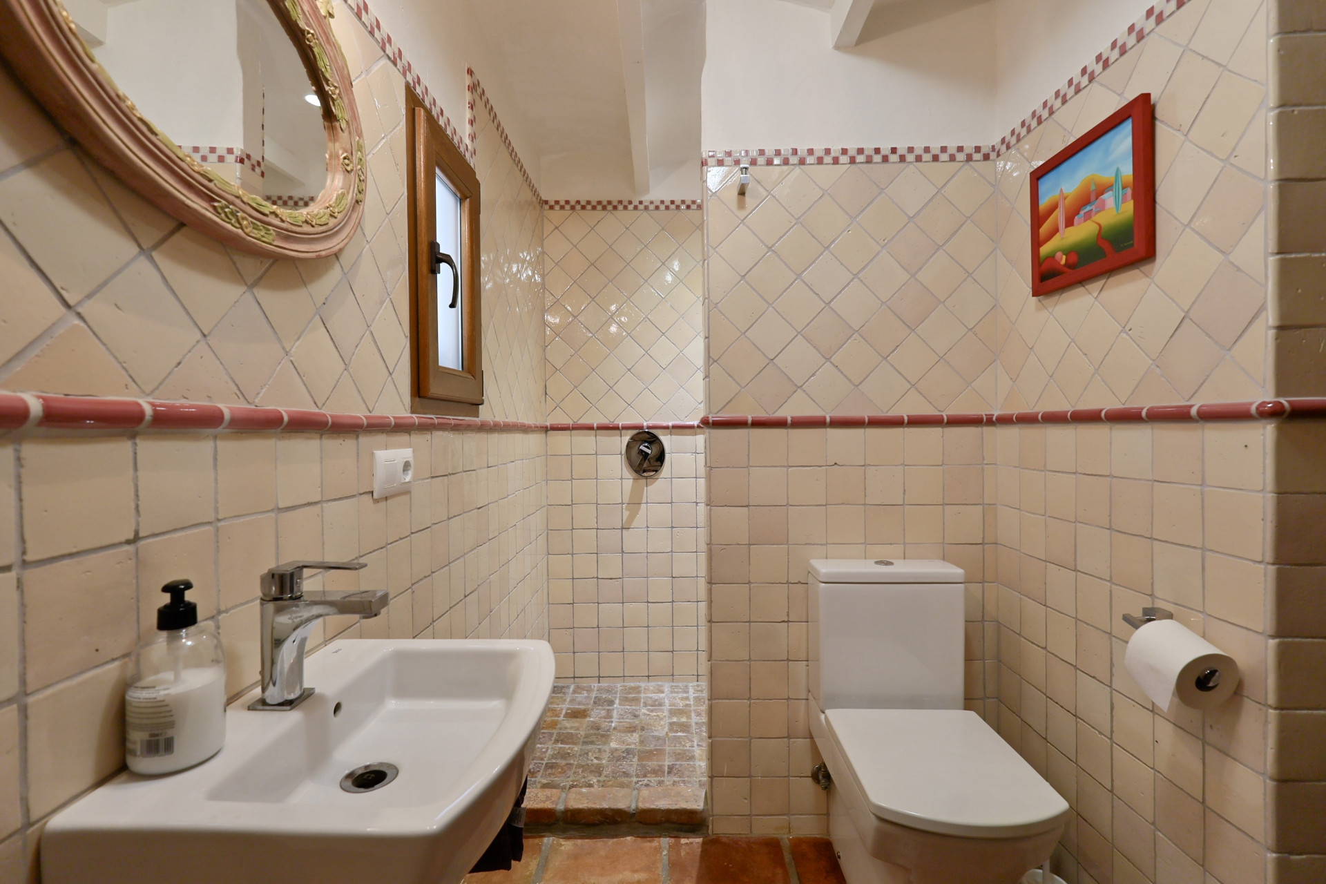 Badkamerdetail met crèmekleurige tegels, ovale spiegel en witte wastafel in Villa in Jávea.