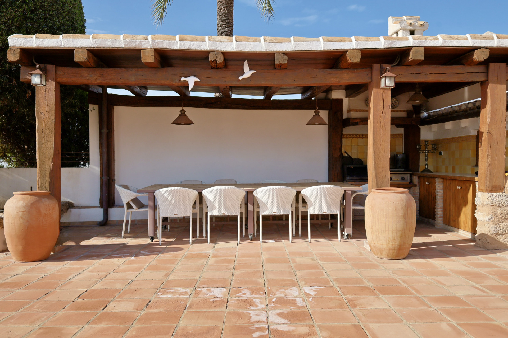 Detail van het overdekte terras met eettafel, wicker stoelen en terracotta tegels.