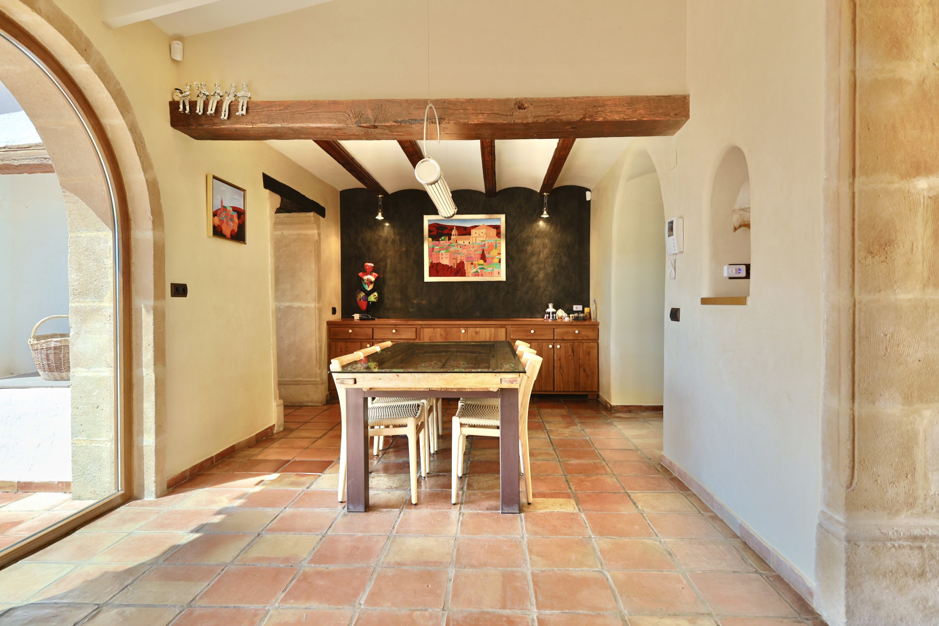 Lichte eetkamer met terracotta vloer en houten balken, tafel met glazen blad.