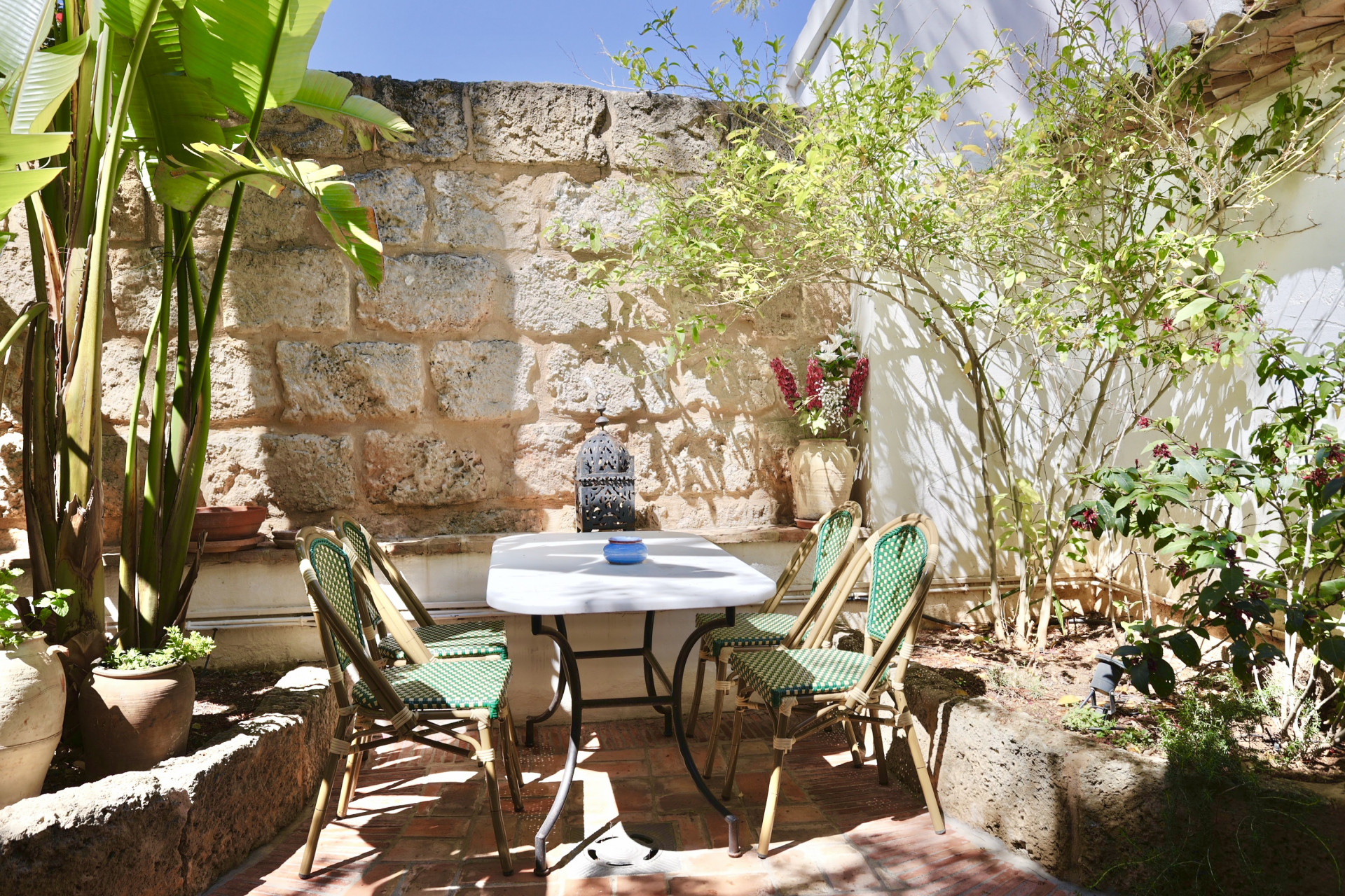 Patio met marmeren tafel, rotan stoelen en rustieke stenen muur. Rustige, natuurlijke sfeer.