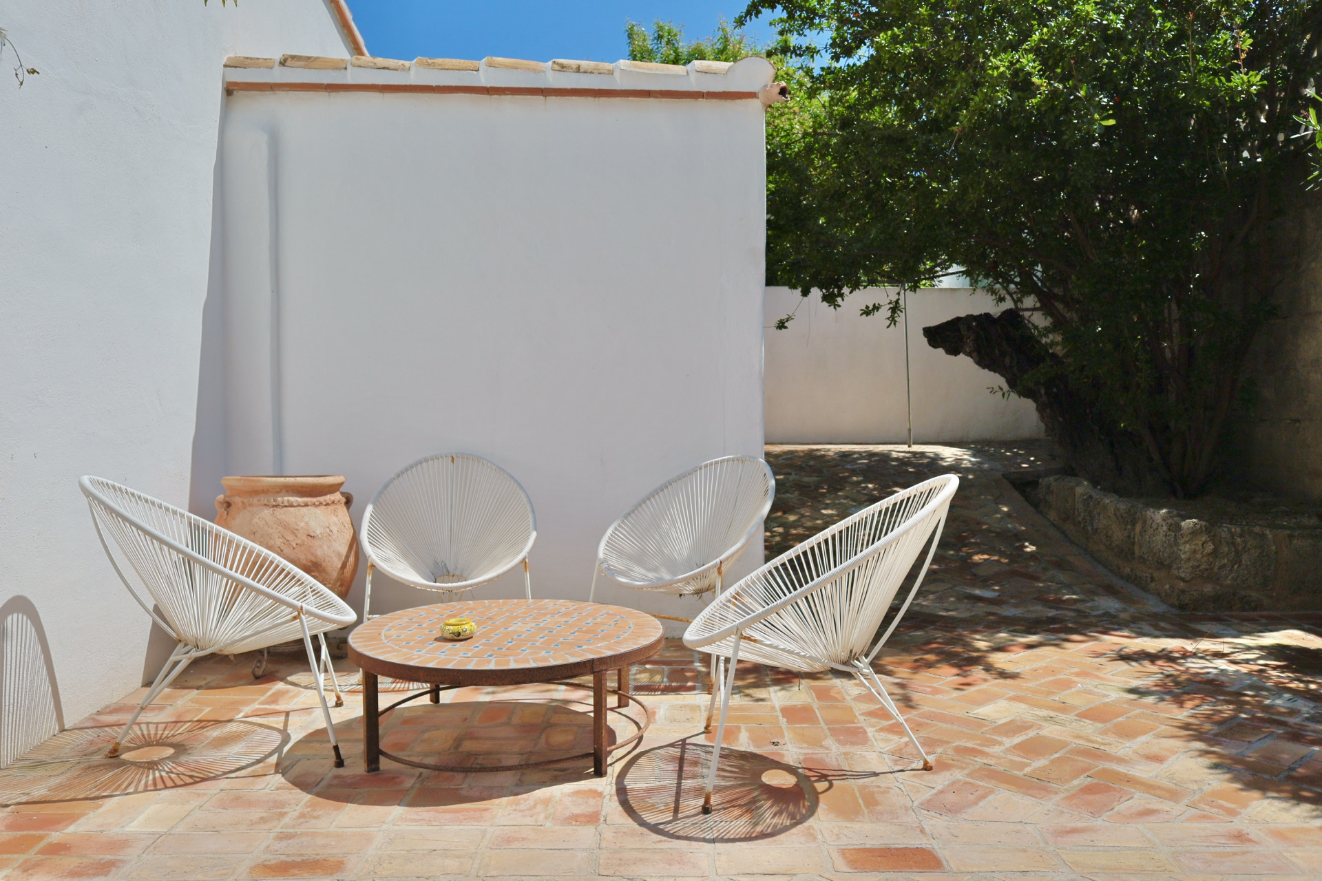 Patio met terracotta vloer, witte touwstoelen en een mozaïektafel, ideaal om buiten te ontspannen.