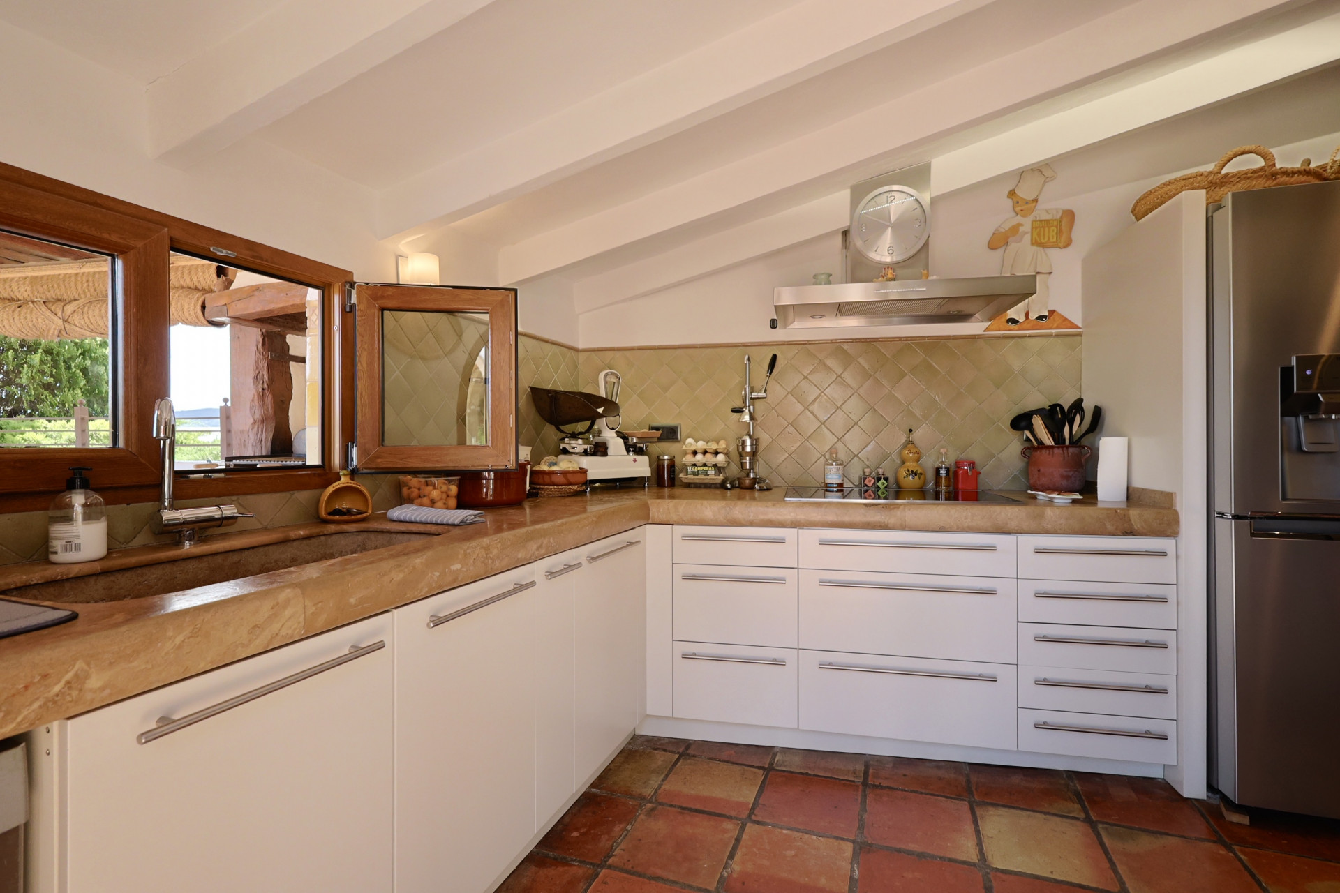 Rustieke keuken met stenen aanrecht, witte kasten en terracotta vloer. Stenen gootsteen met houten raam.