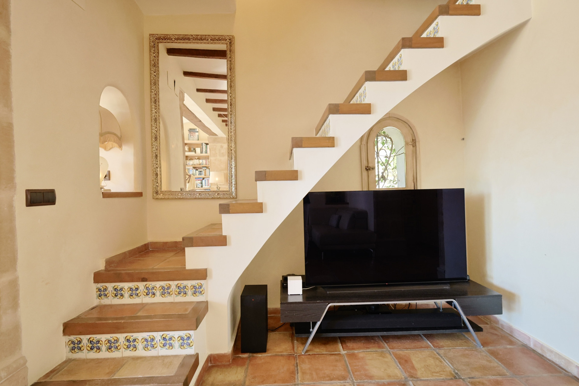 Trapdetail met decoratieve tegels en tv in woonkamer met terracotta vloer.