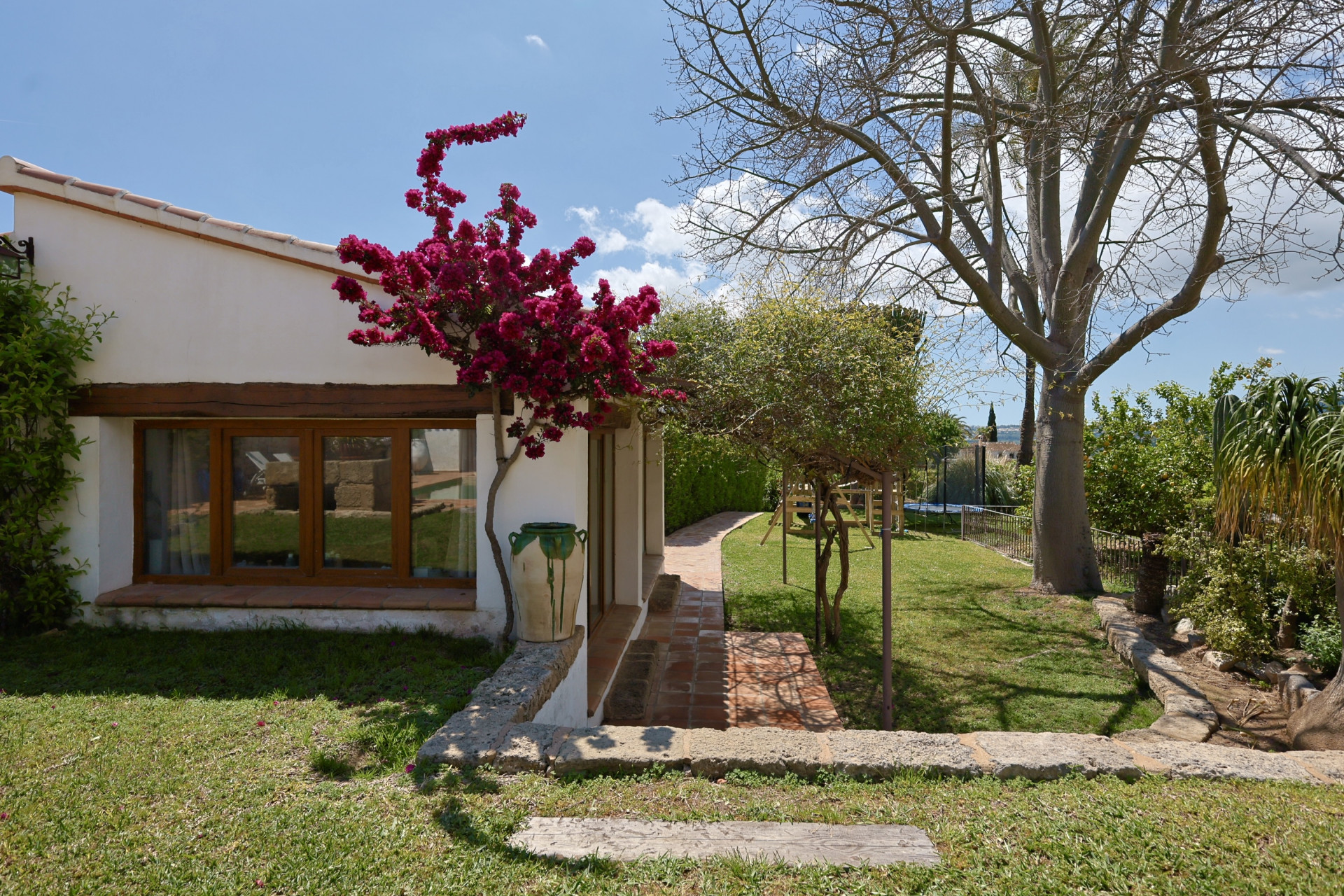 Tuinzicht met fuchsia bougainvillea die tegen de gevel van de villa in Jávea klimt. Raam met houten frame.