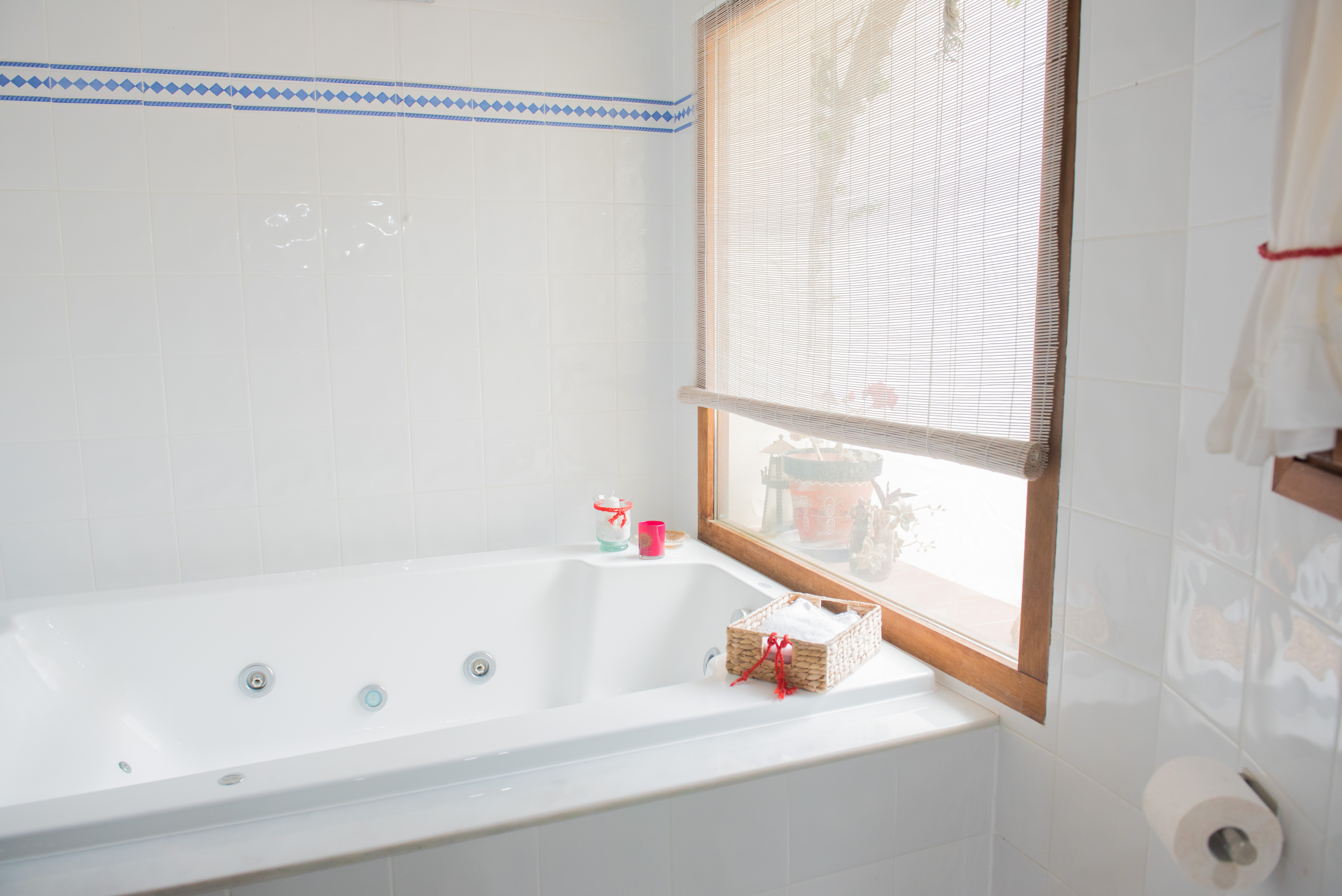 Badkamer voorzien van een whirlpool ligbad, witte wandtegels met een blauwe sierrand en een houten raamkozijn met natuurlijk lichtinval.