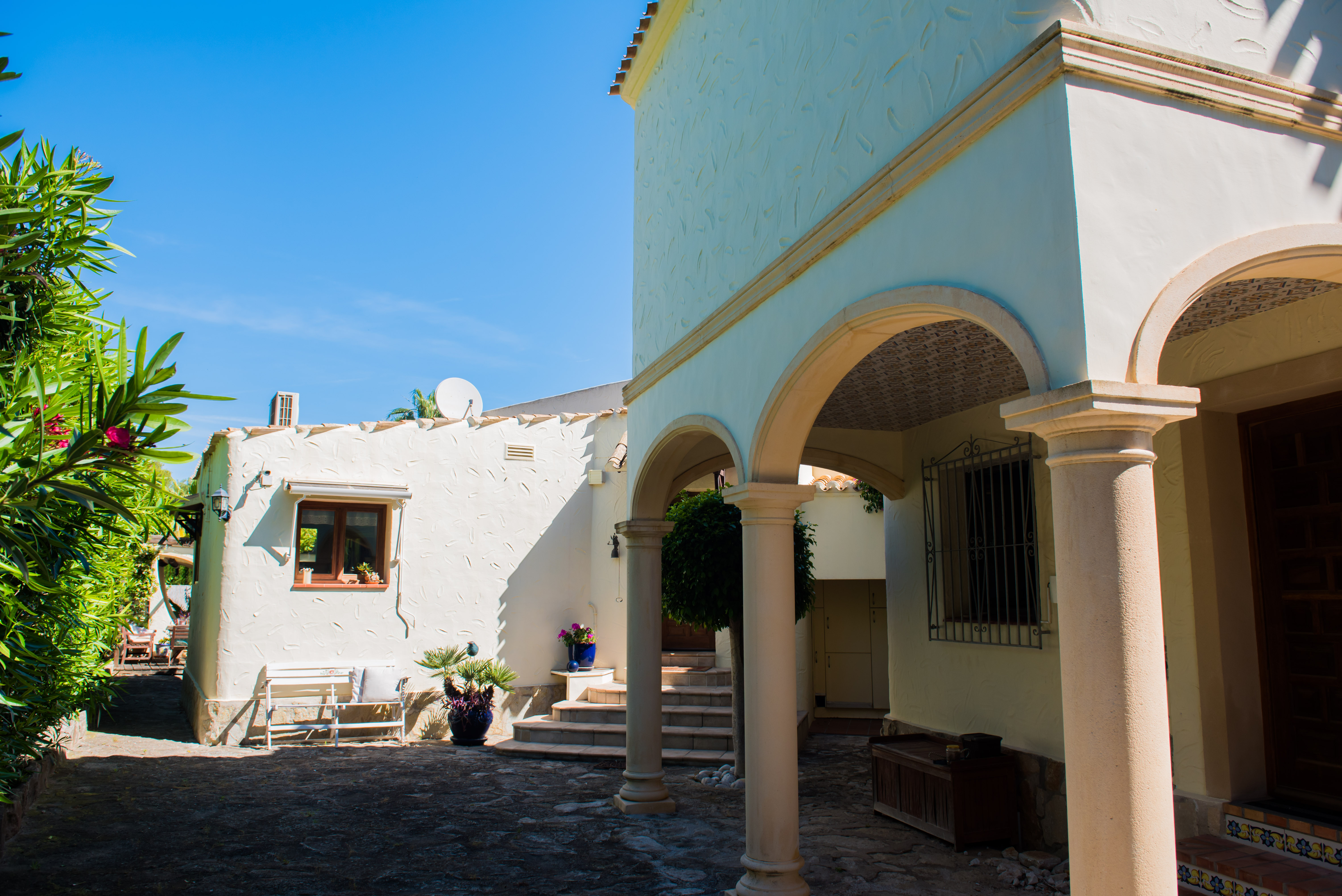 Buitenaanzicht van de villa met stenen bogen en witte, gestructureerde muren, omgeven door mediterraan groen.