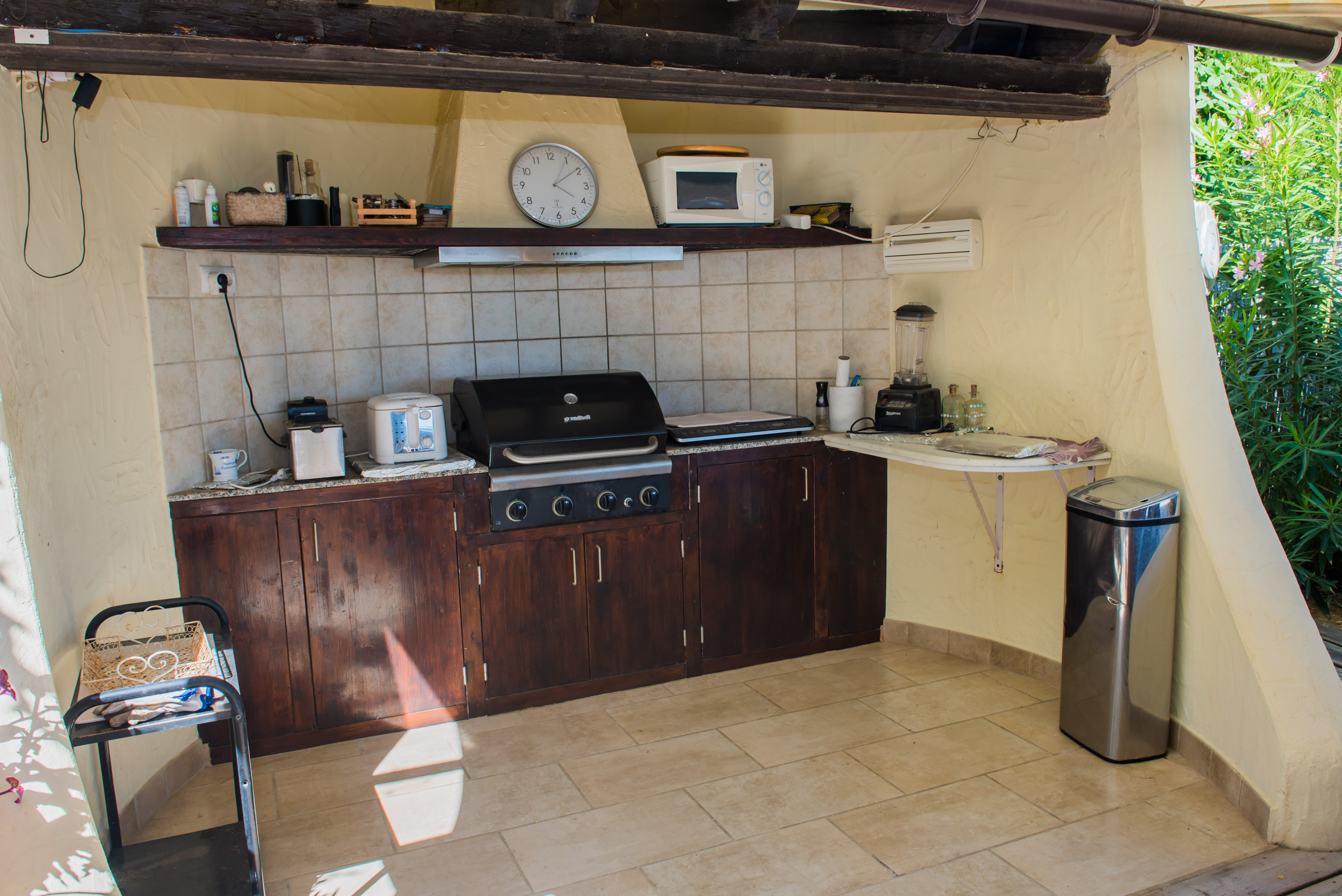 Buitenkeuken uitgerust met een grill, donkerhouten aanrecht en apparatuur.
