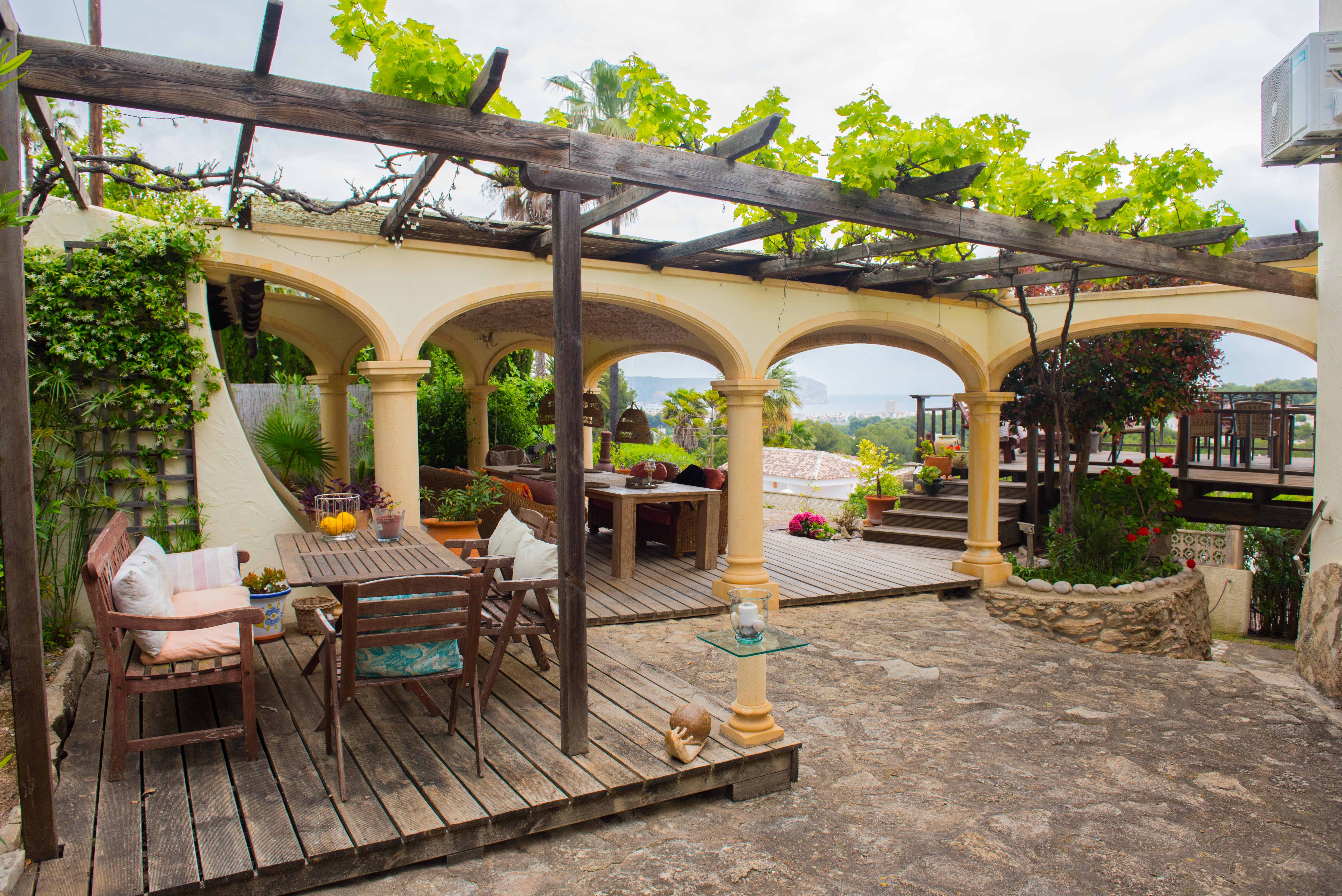 Buitenterras met houten pergola en klimplanten, houten vlonders en een bogen galerij met weids uitzicht over de zee en de kustlijn.