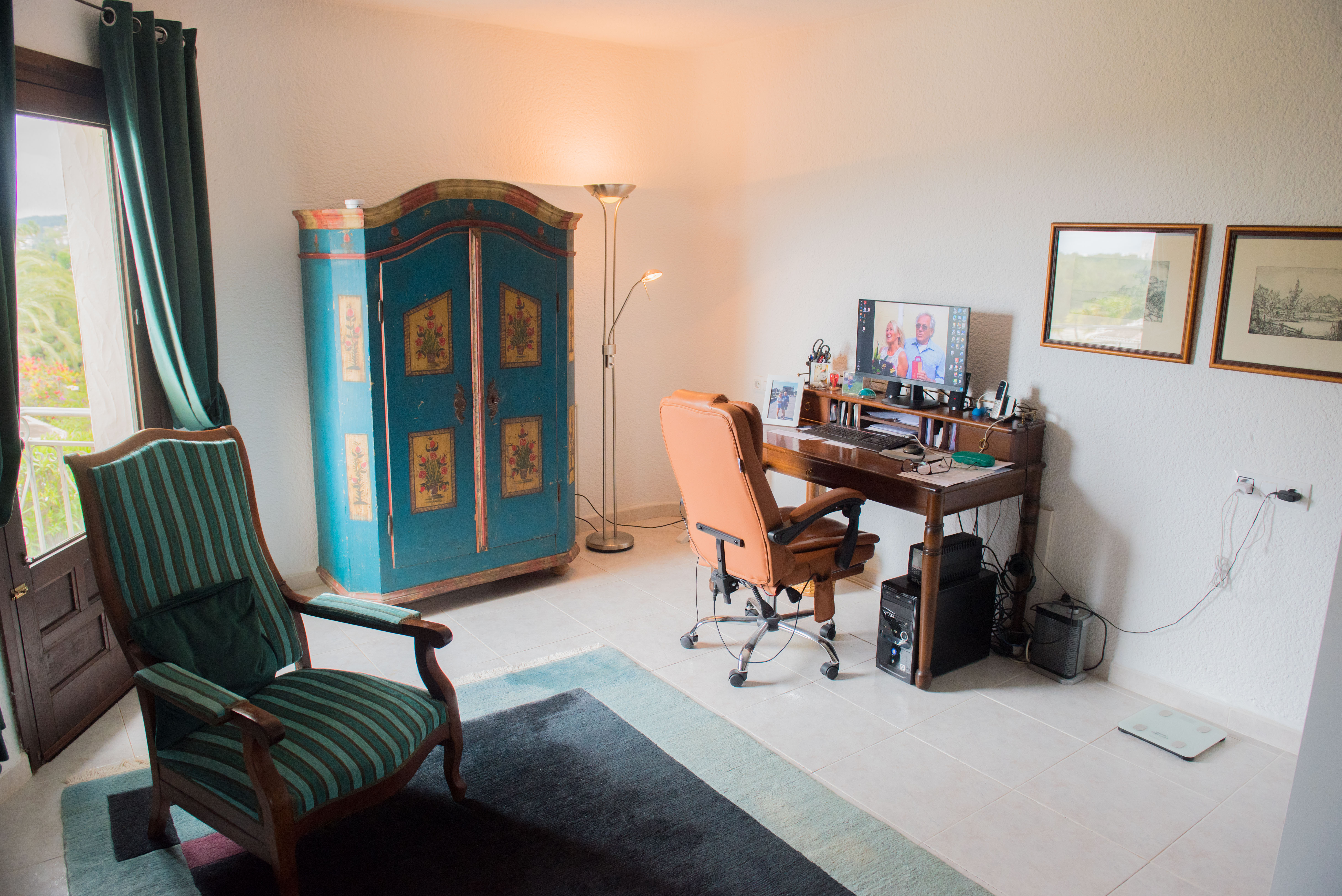 Functionele werkkamer met klassiek houten bureau, gedecoreerde rustieke kast en lederen stoel. Voorzien van natuurlijk licht en directe toegang tot het terras.