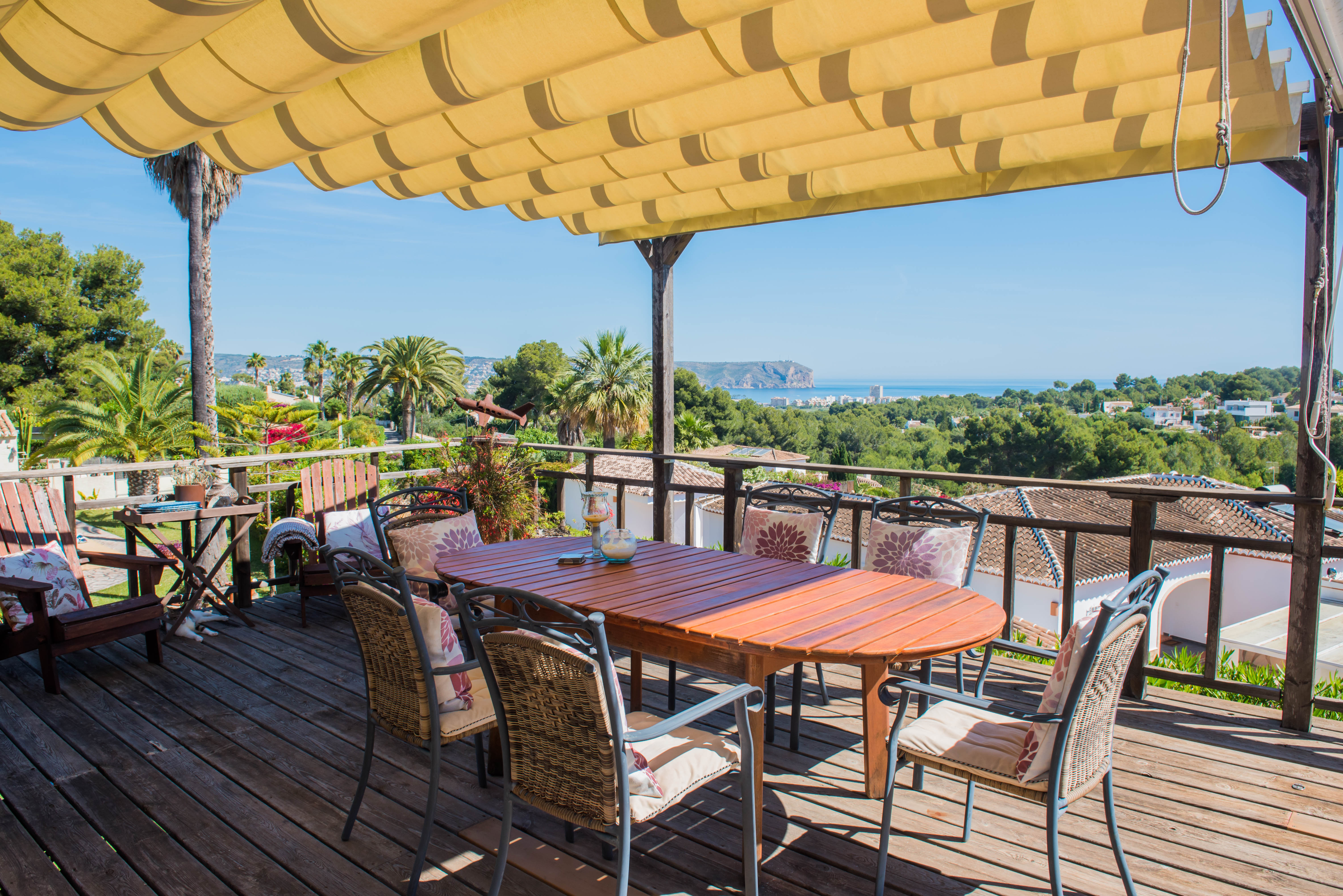 Houten terras met luifel en eettafel, met uitzicht op de zee en weelderig groen.