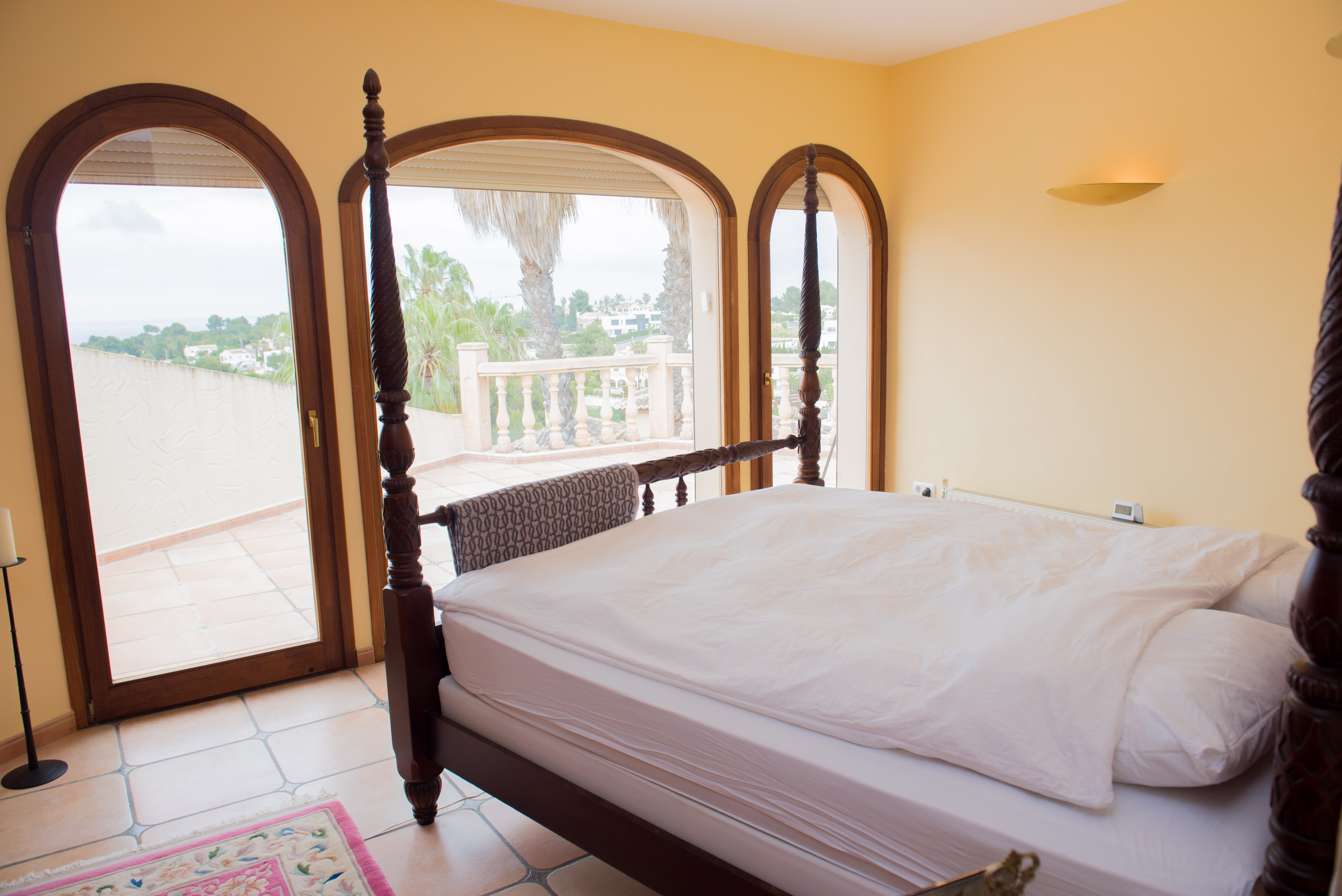Master suite met een donkerhouten hemelbed en halfronde openslaande deuren naar een terras met uitzicht over de mediterrane omgeving.
