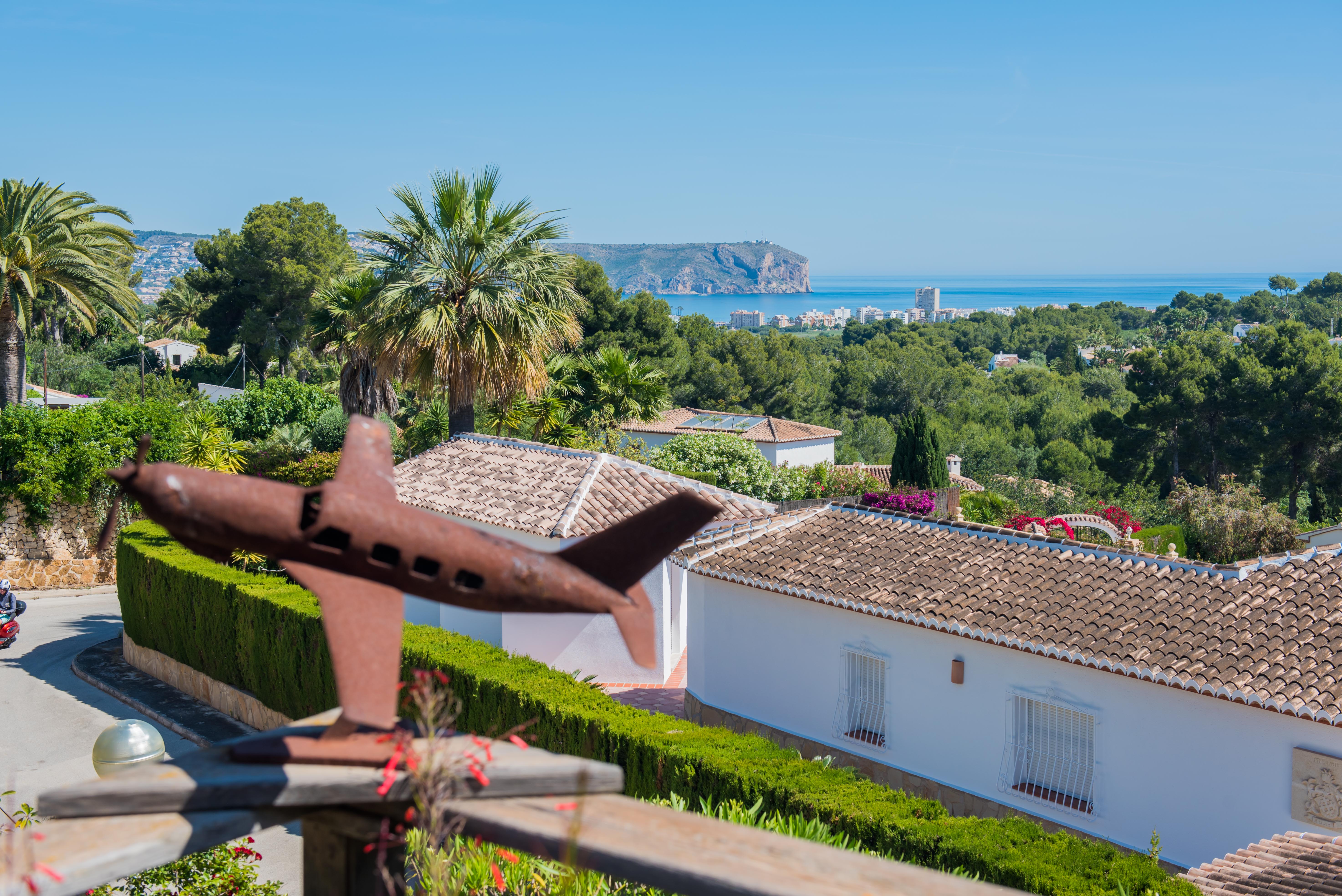 Panoramisch uitzicht op Jávea vanaf het terras, met een vliegtuigsculptuur op de voorgrond en weelderig groen.