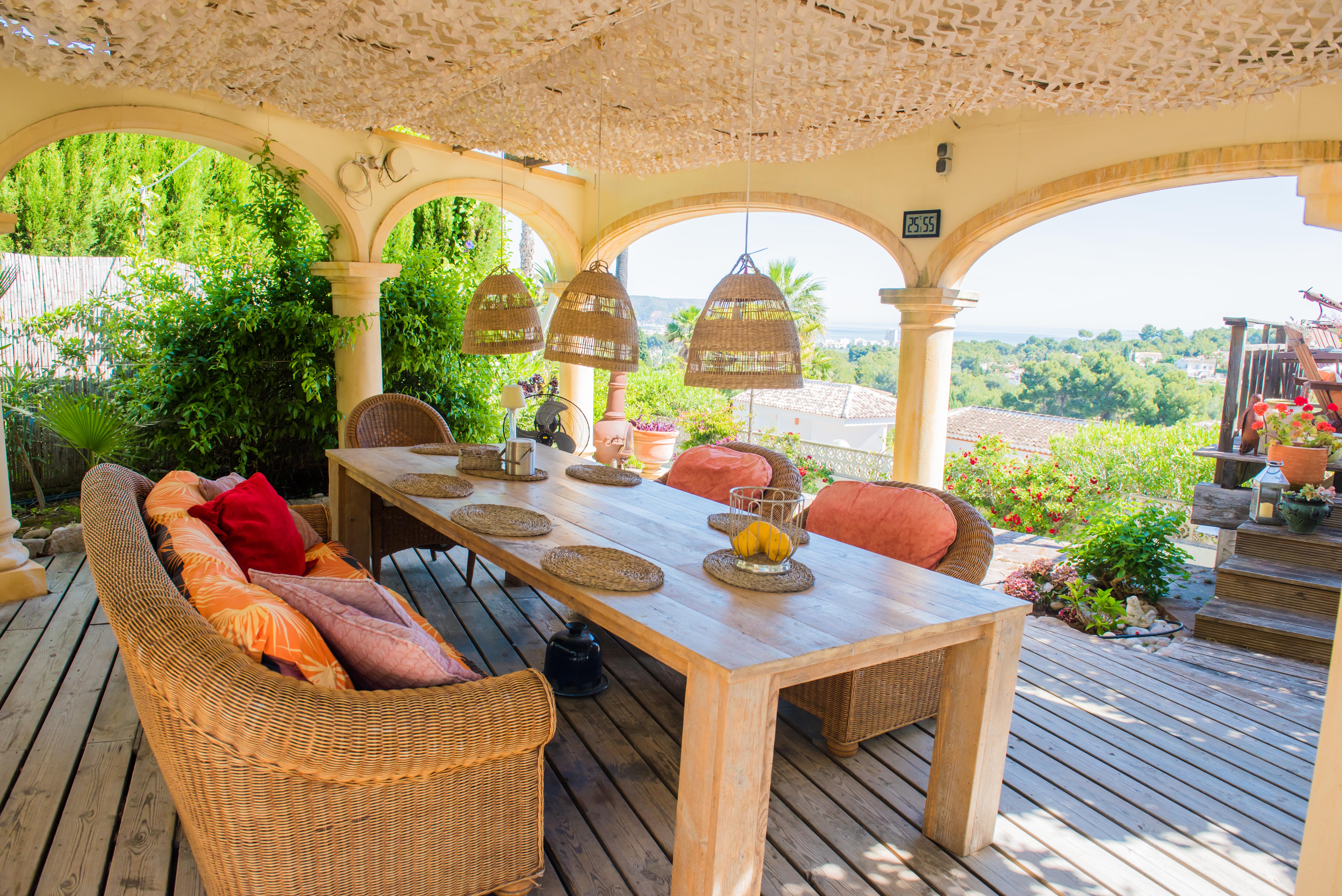 Porch met rustieke houten tafel en rieten stoelen, met panoramisch uitzicht op de tuin en de Middellandse Zee.