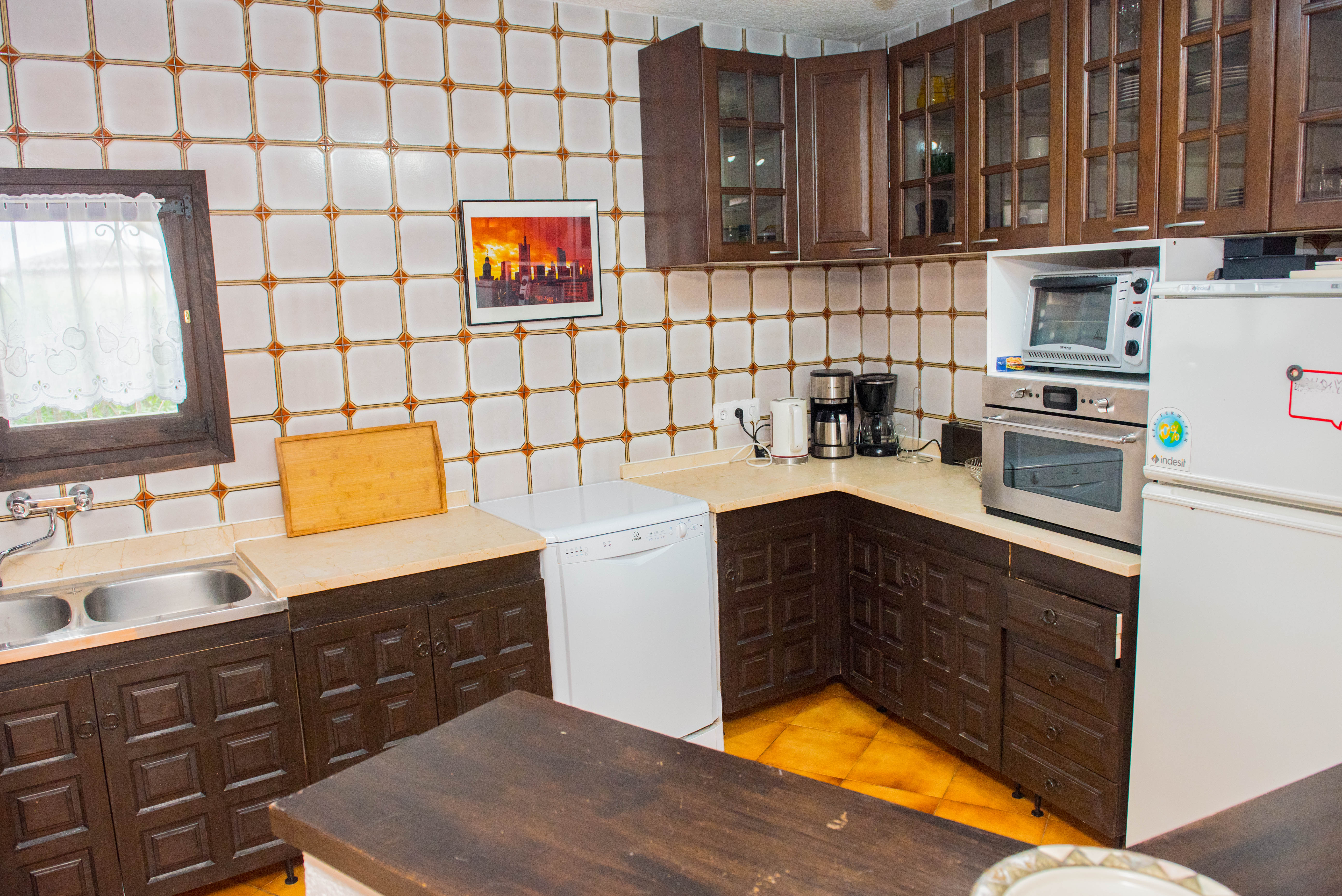 Rustieke keuken met donkerhouten kasten, een crème werkblad en gedecoreerde wandtegels. Voorzien van een witte vaatwasser, koelkast en ingebouwde oven.