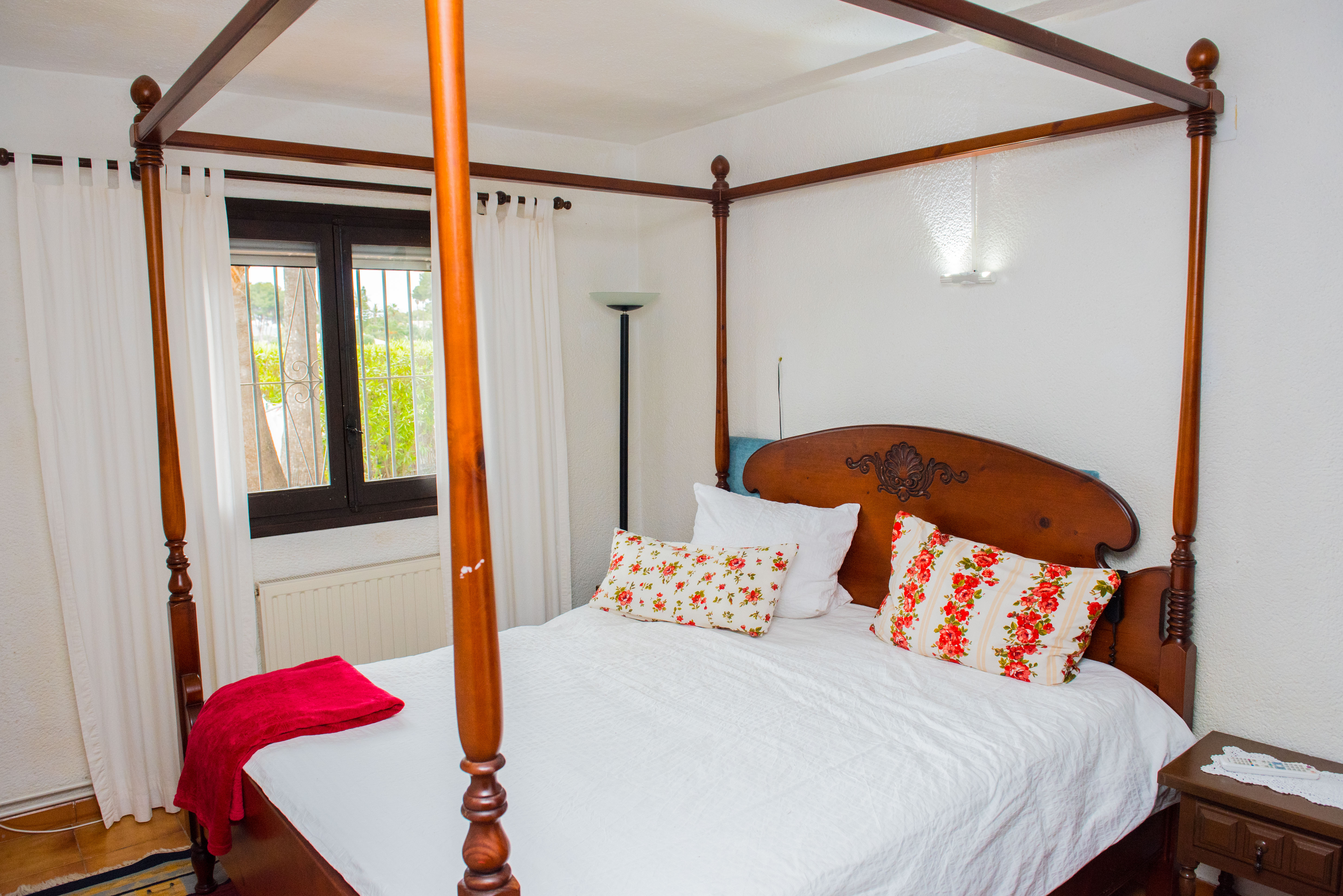 Slaapkamer met een bewerkt houten hemelbed, bloemenkussens en een raam met uitzicht op de tuin en een radiator.