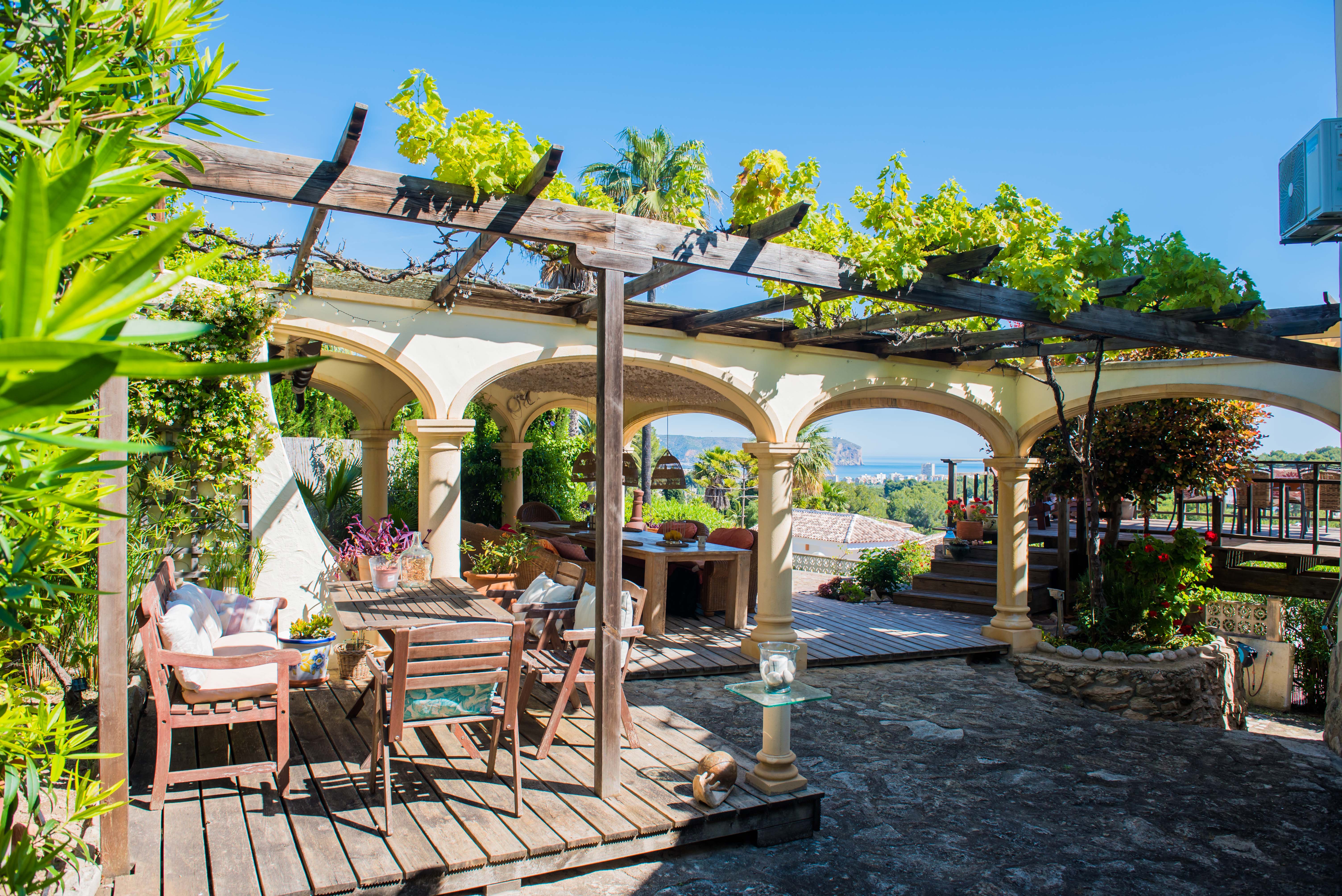 Terras met houten pergola begroeid met groen en stenen bogen met uitzicht op de Middellandse Zee.