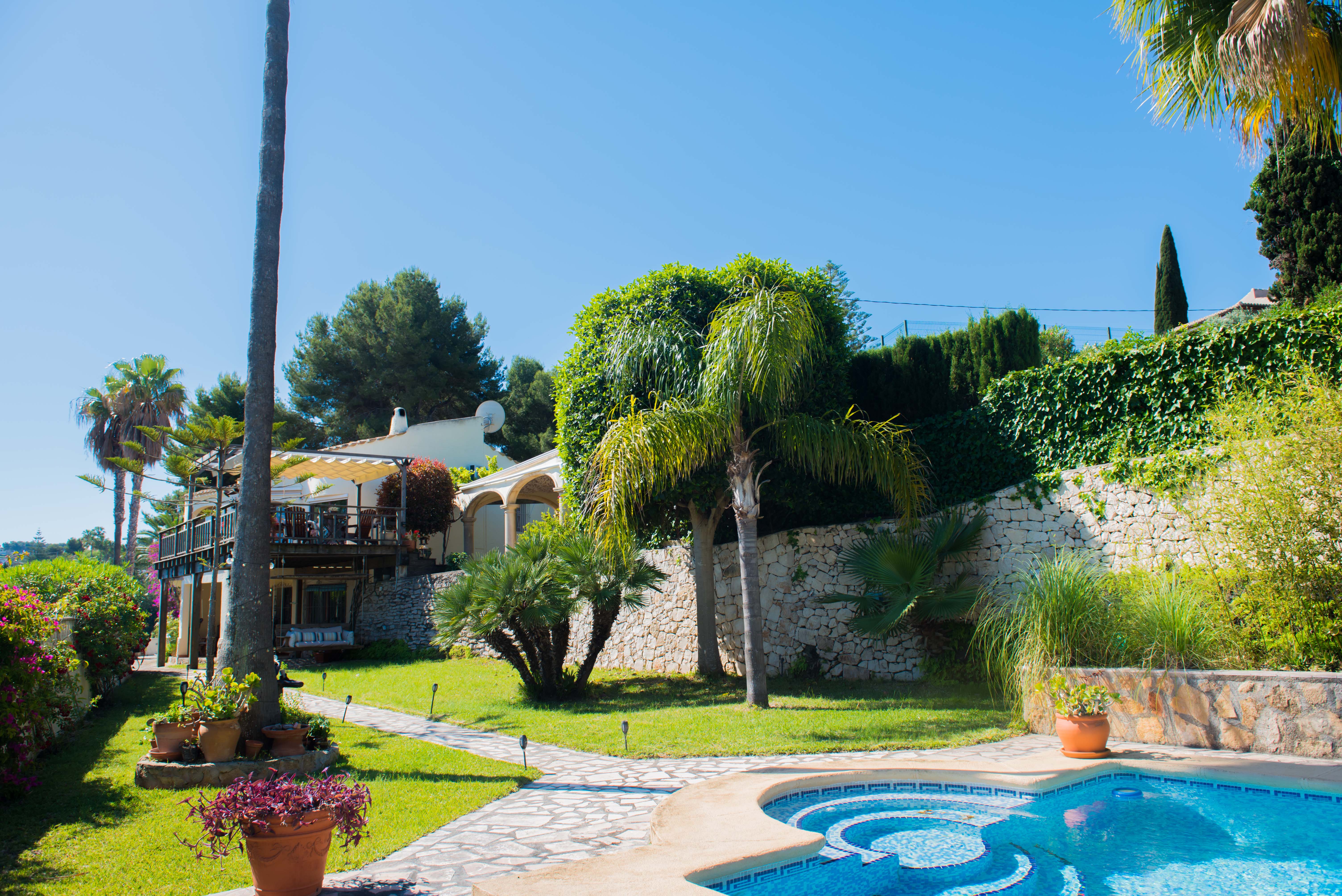 Tuin met blauw mozaïekzwembad en stenen pad dat leidt naar de villa in mediterrane stijl.