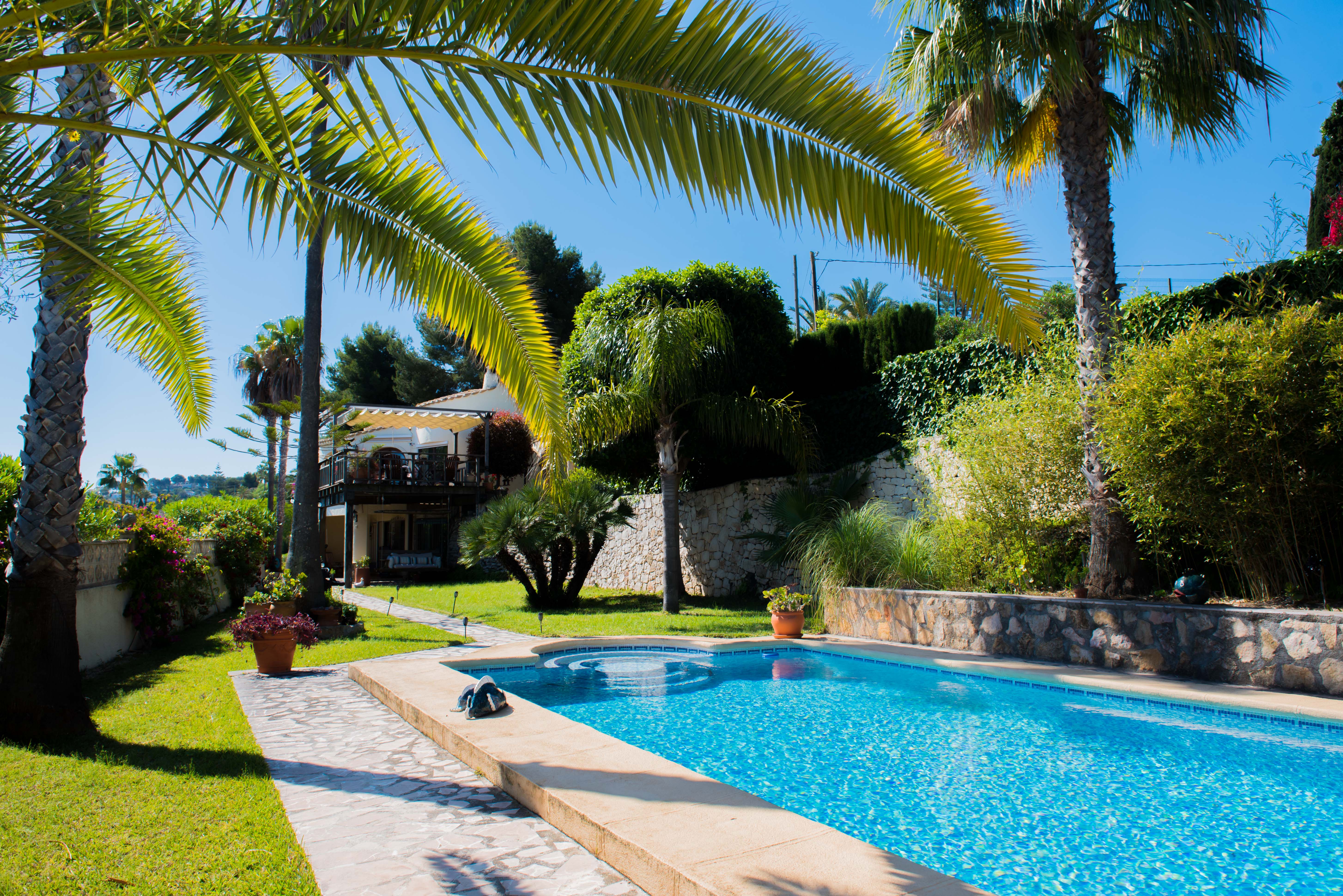 Uitzicht op het blauw betegelde zwembad en de mediterrane tuin met palmbomen in Jávea.