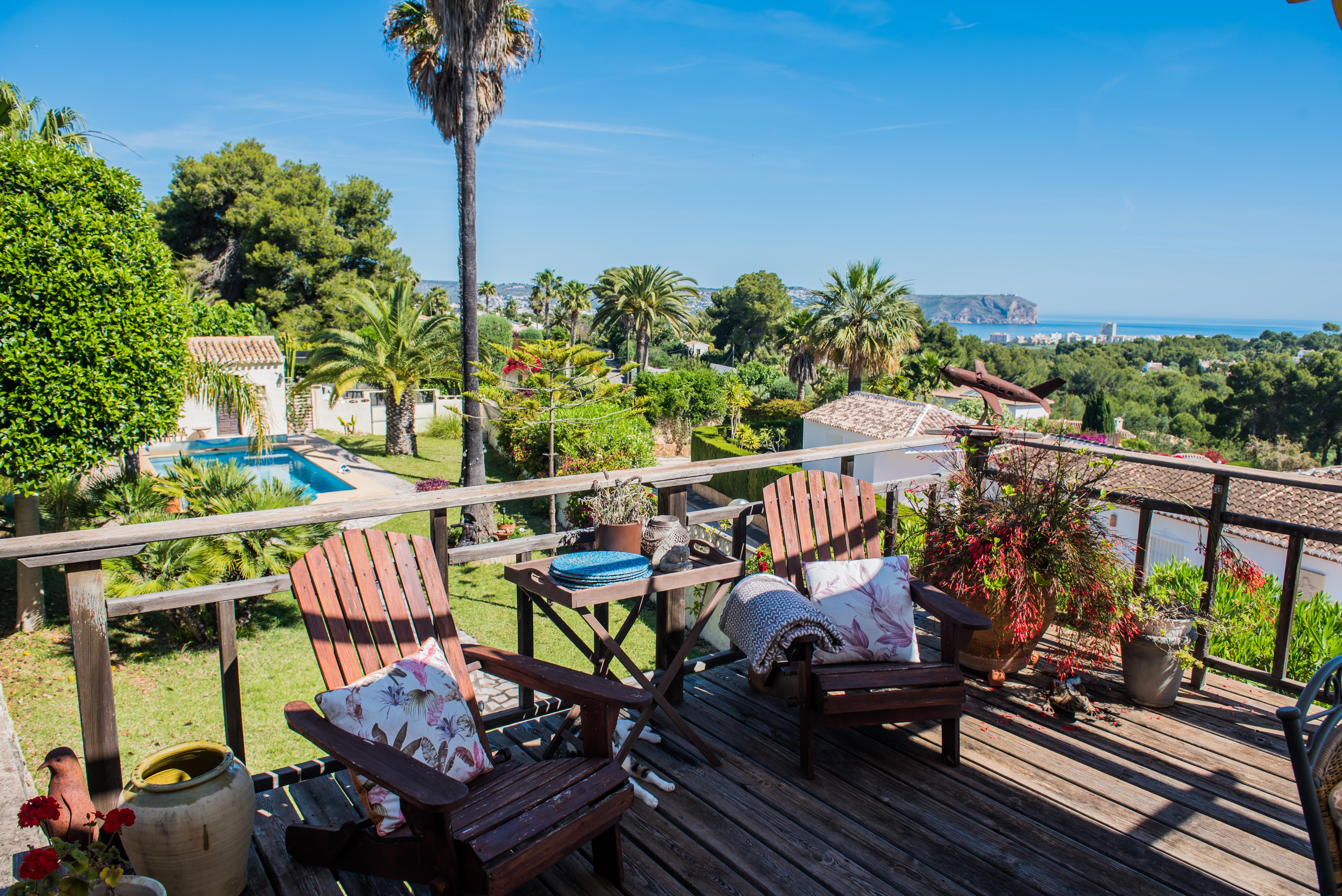 Uitzicht vanaf het houten terras met Adirondack-stoelen, tuinen en panoramisch uitzicht op zee in Jávea.