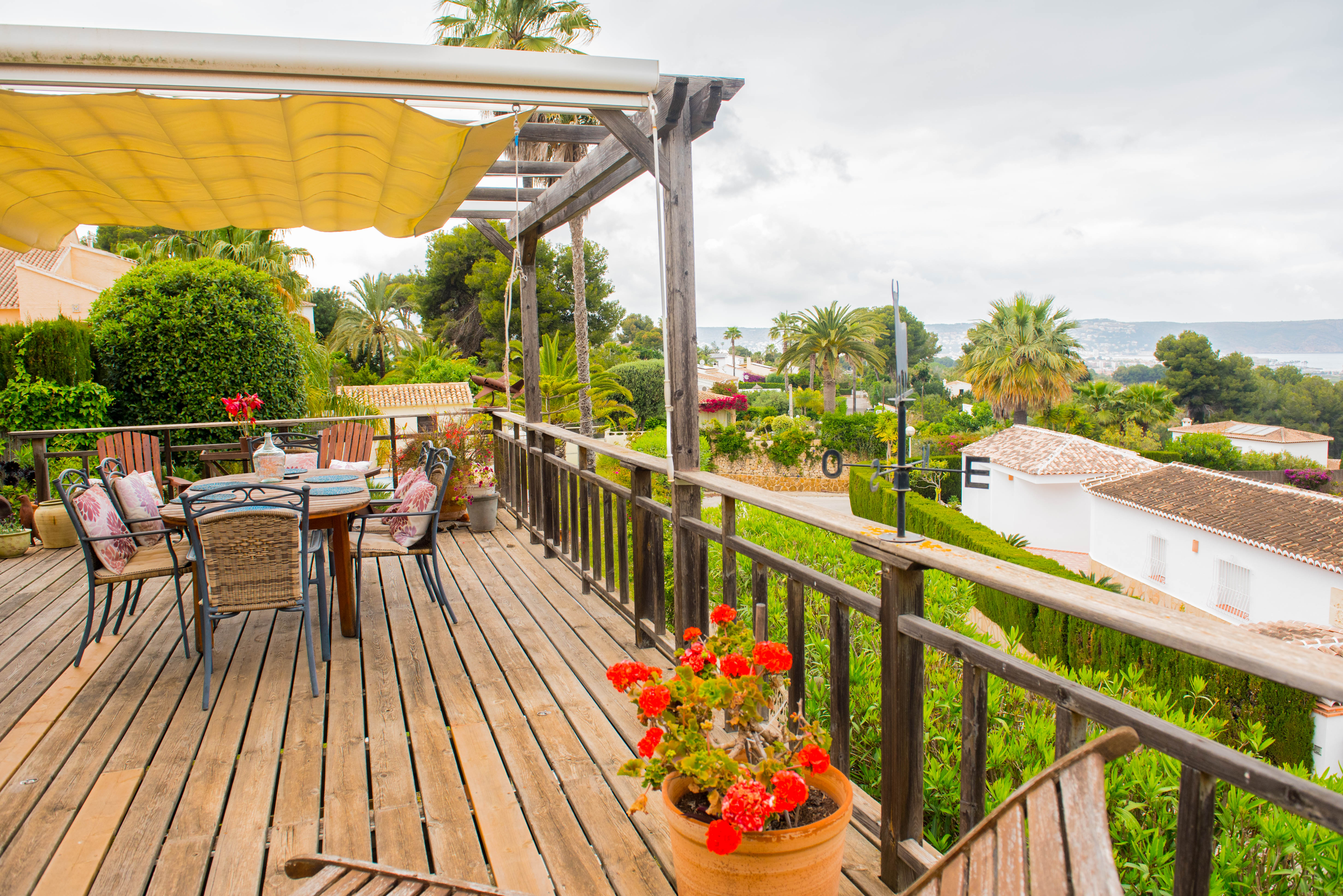 Verhoogd houten terras met uitschuifbaar zonnescherm, eethoek buiten en rustieke balustrade met panoramisch uitzicht op de zee en de omgeving.