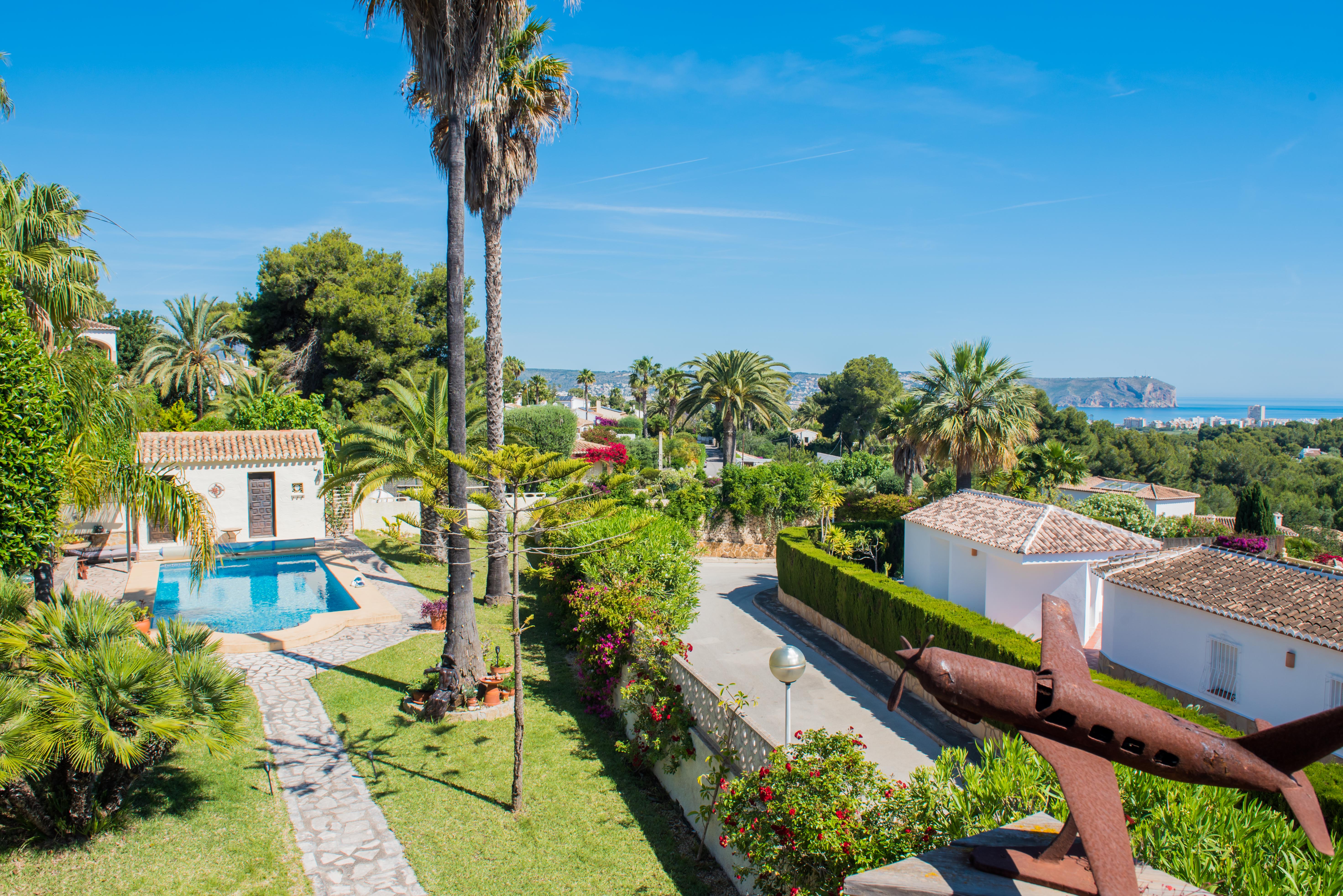 Verhoogd uitzicht op de mediterrane tuin met zwembad en roestige vliegtuigsculptuur in Jávea.
