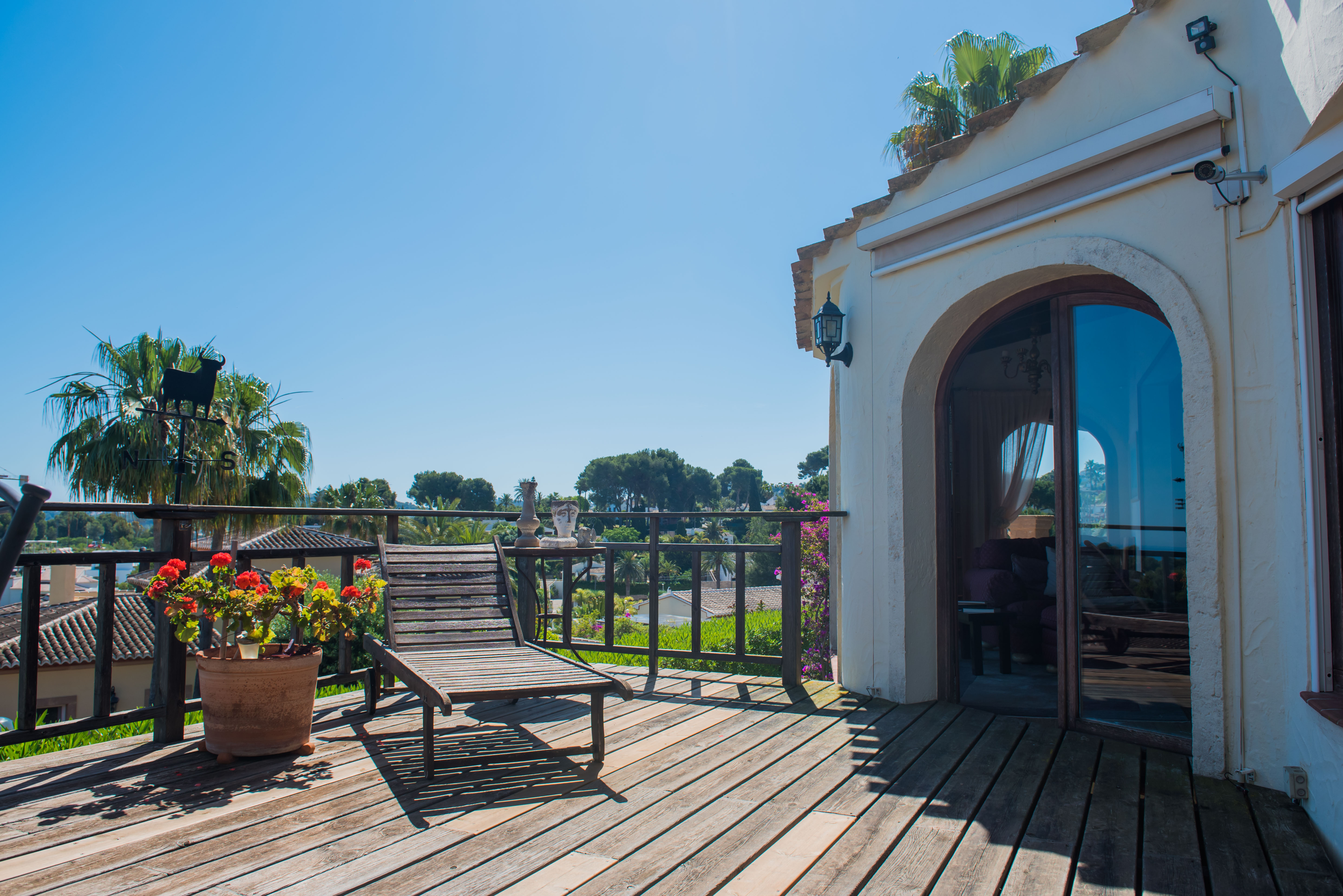 Zonnig terras met houten vloer, een ligstoel en uitzicht op het mediterrane landschap.