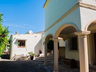 Buitenaanzicht van de villa met stenen bogen en witte, gestructureerde muren, omgeven door mediterraan groen.