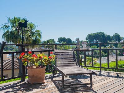 Houten terras met ligstoel, uitzicht op de tuin en decoratieve details zoals een stierenwindvaan en geraniumpotten.