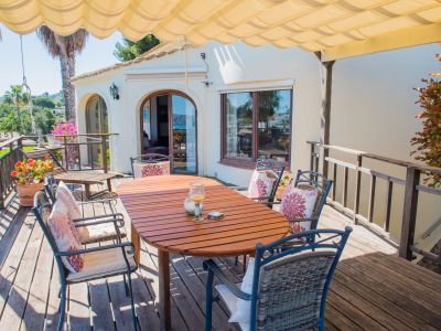 Overdekt terras met houten tafel en gestoffeerde stoelen, ideaal om te genieten van een panoramisch uitzicht op de Middellandse Zee.