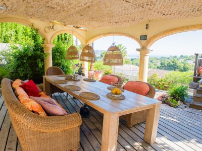 Porch met rustieke houten tafel en rieten stoelen, met panoramisch uitzicht op de tuin en de Middellandse Zee.