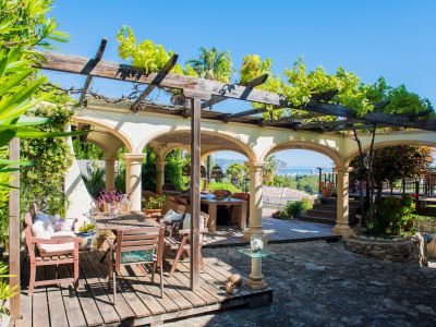 Terras met houten pergola begroeid met groen en stenen bogen met uitzicht op de Middellandse Zee.