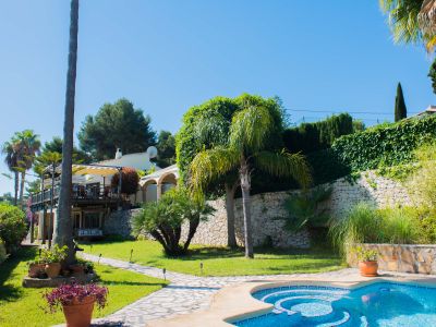 Tuin met blauw mozaïekzwembad en stenen pad dat leidt naar de villa in mediterrane stijl.